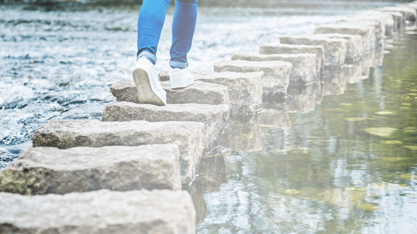 person walking across stepping stones in water that's calm on one side and rushing on the other