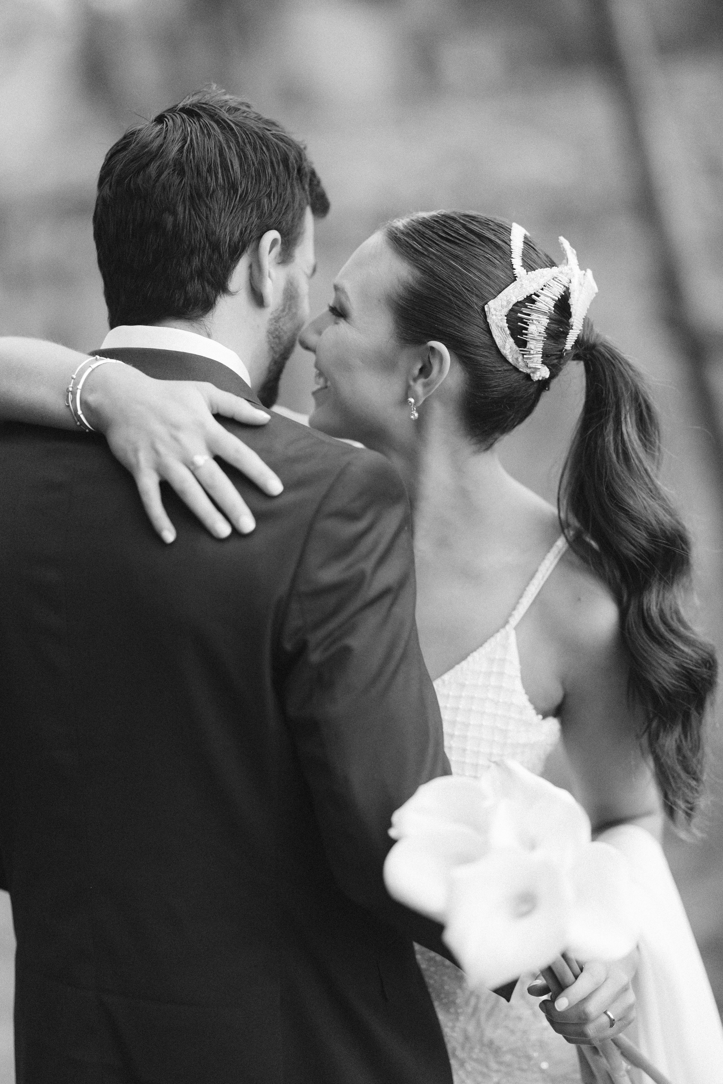 Una pareja de novios bailando en su boda, la mujer sostiene un ramo de flores y ambos sonríen, en una fotografía en blanco y negro.