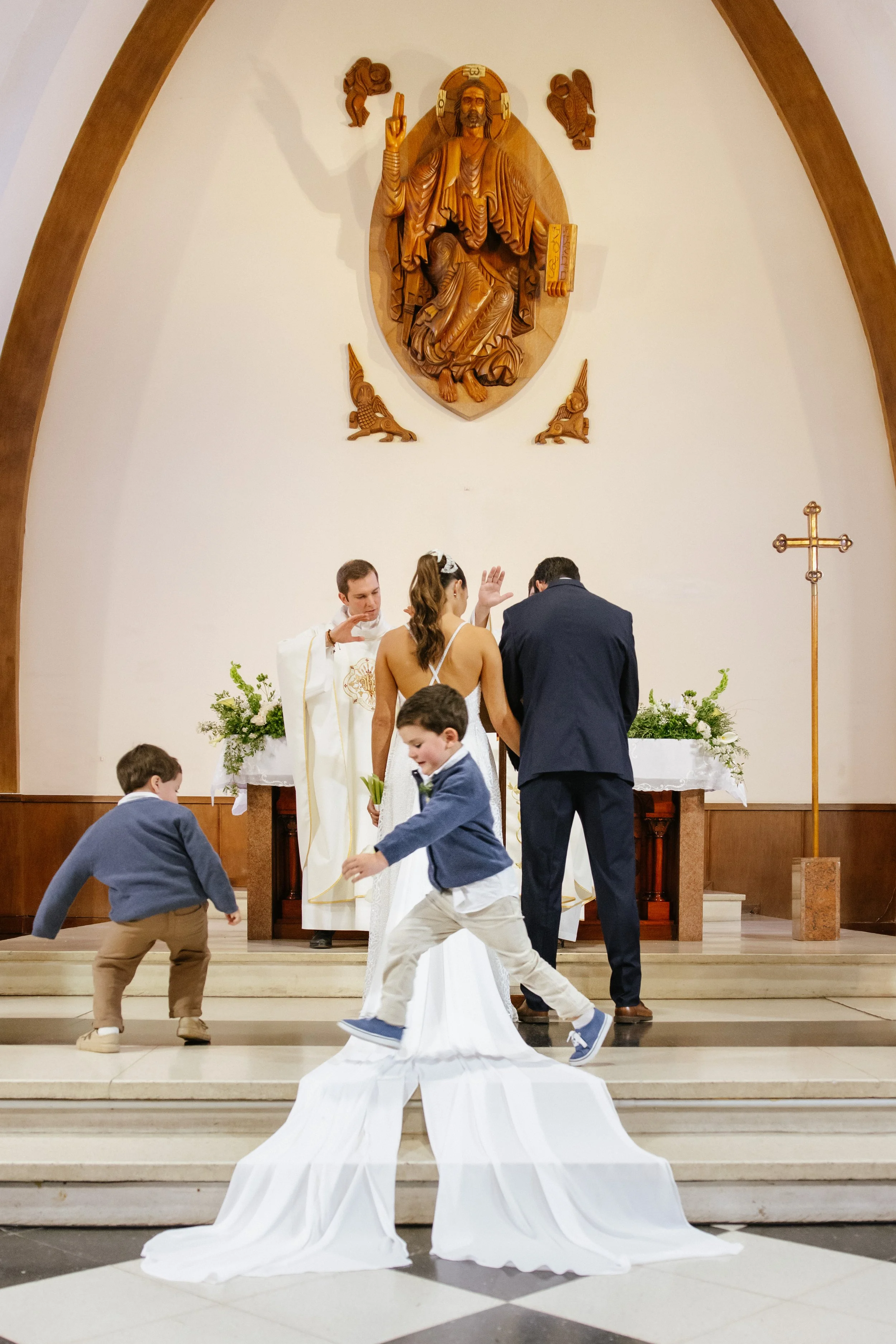 Una ceremonia religiosa en una iglesia con figuras de niños bailando y un altar con una figura de Jesucristo en el fondo.