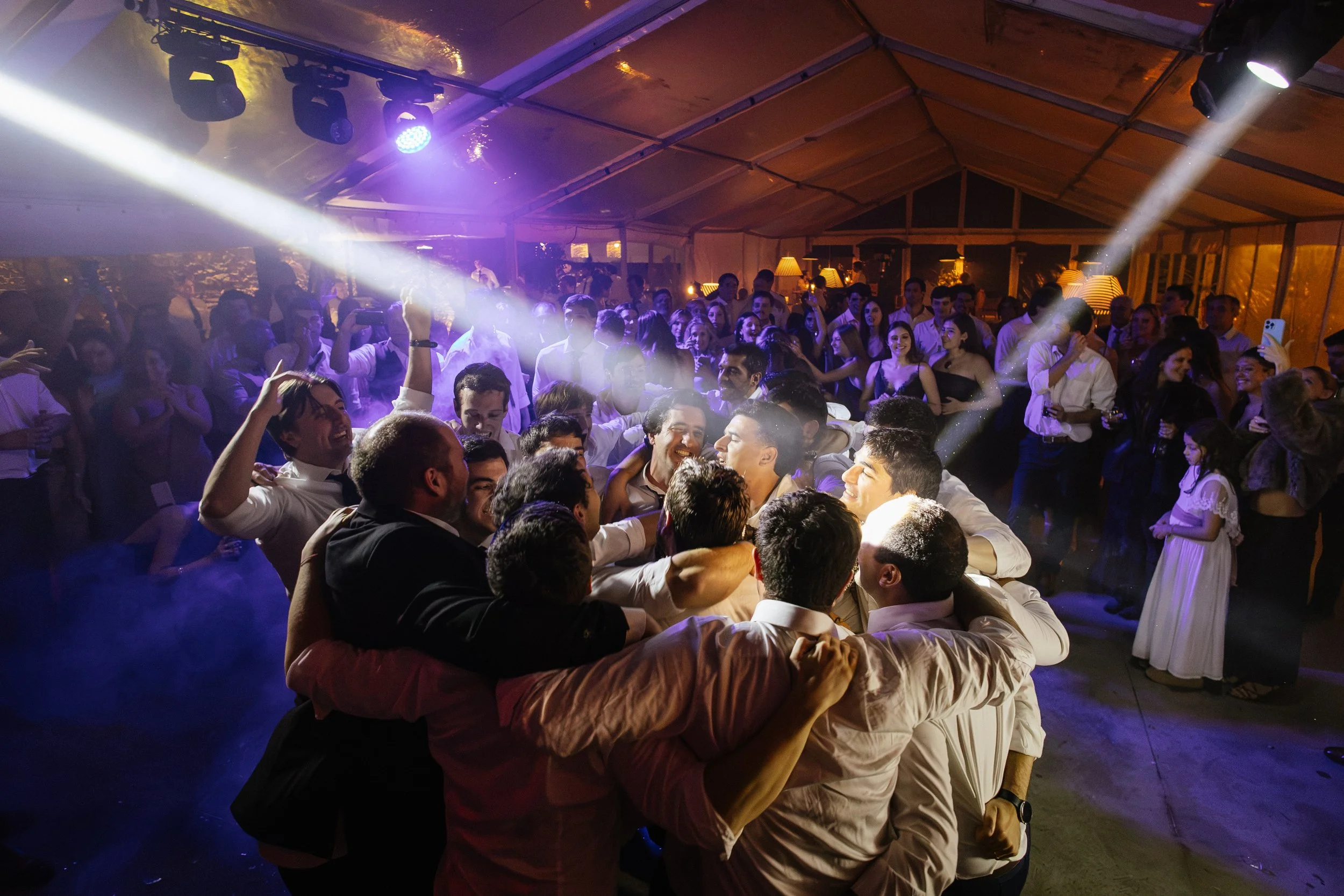Grupo de personas bailando y disfrutando en una fiesta con iluminación colorida en un espacio con techo de lona.