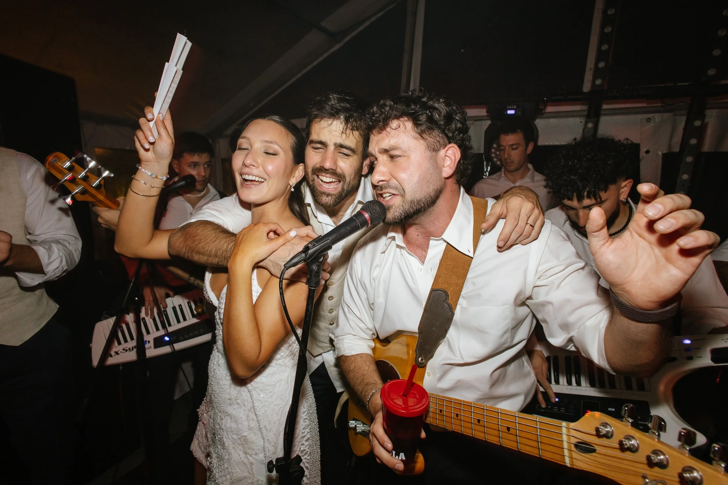 Grupo de personas cantando y tocando instrumentos en una fiesta o concierto, ambiente animado y alegre.