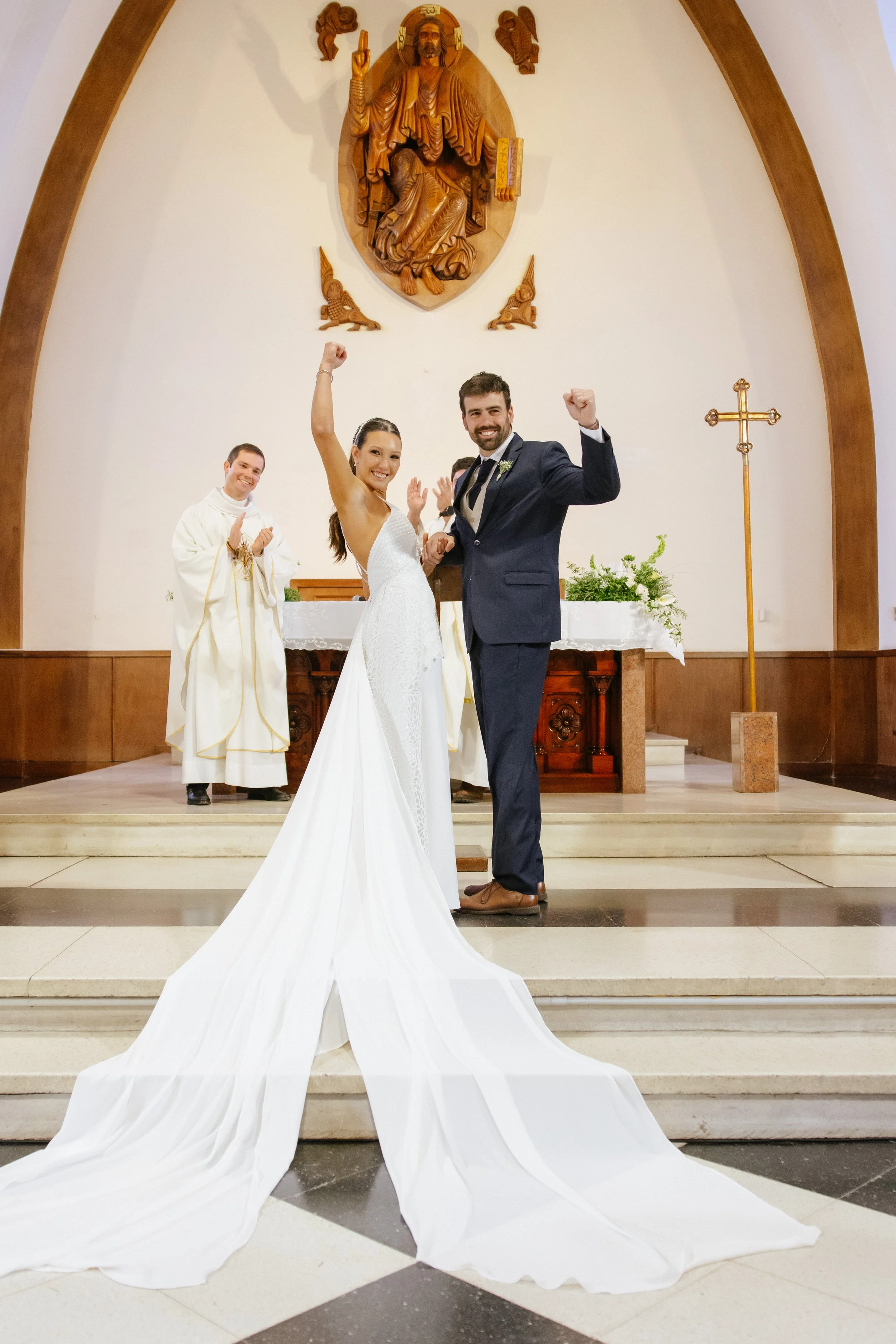 Pareja de recién casados en la iglesia, celebrando su boda con sacerdote y bíblica, vestido de novia y traje formal, ante altar y símbolo religioso.