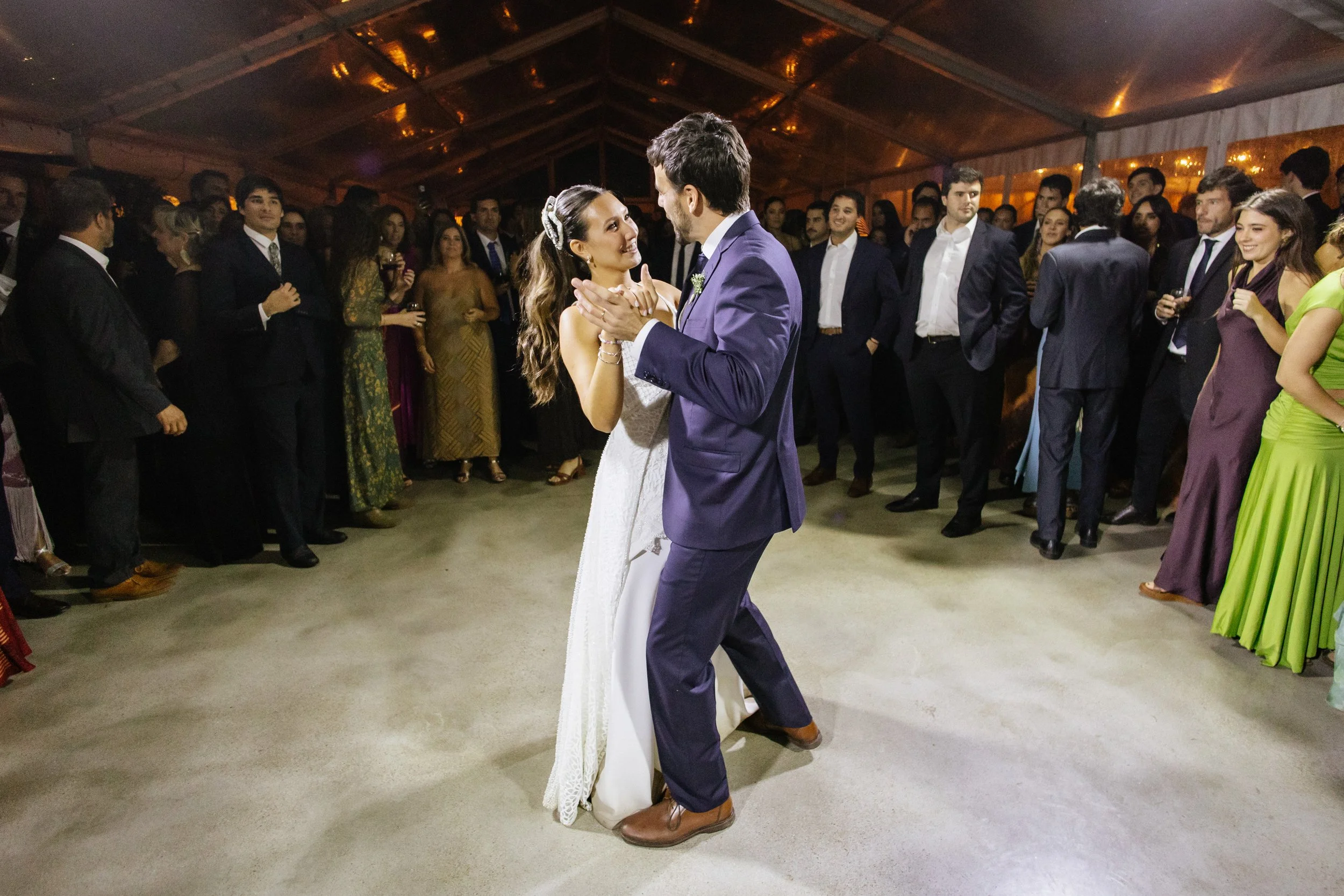 Pareja bailando en una boda, rodeados de invitados en un espacio cubierto con techo de madera