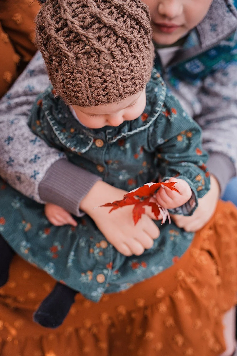 A baby girl dressed in fall colors holds a red leaf in autumn during her photo session in Lancaster, PA