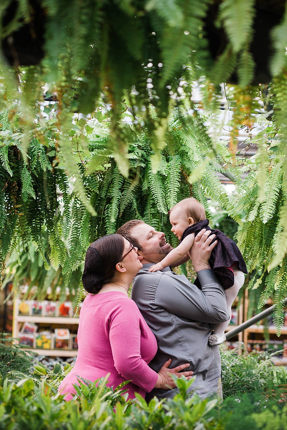  Mother and Father holding up their baby girl in a greenhouse. 