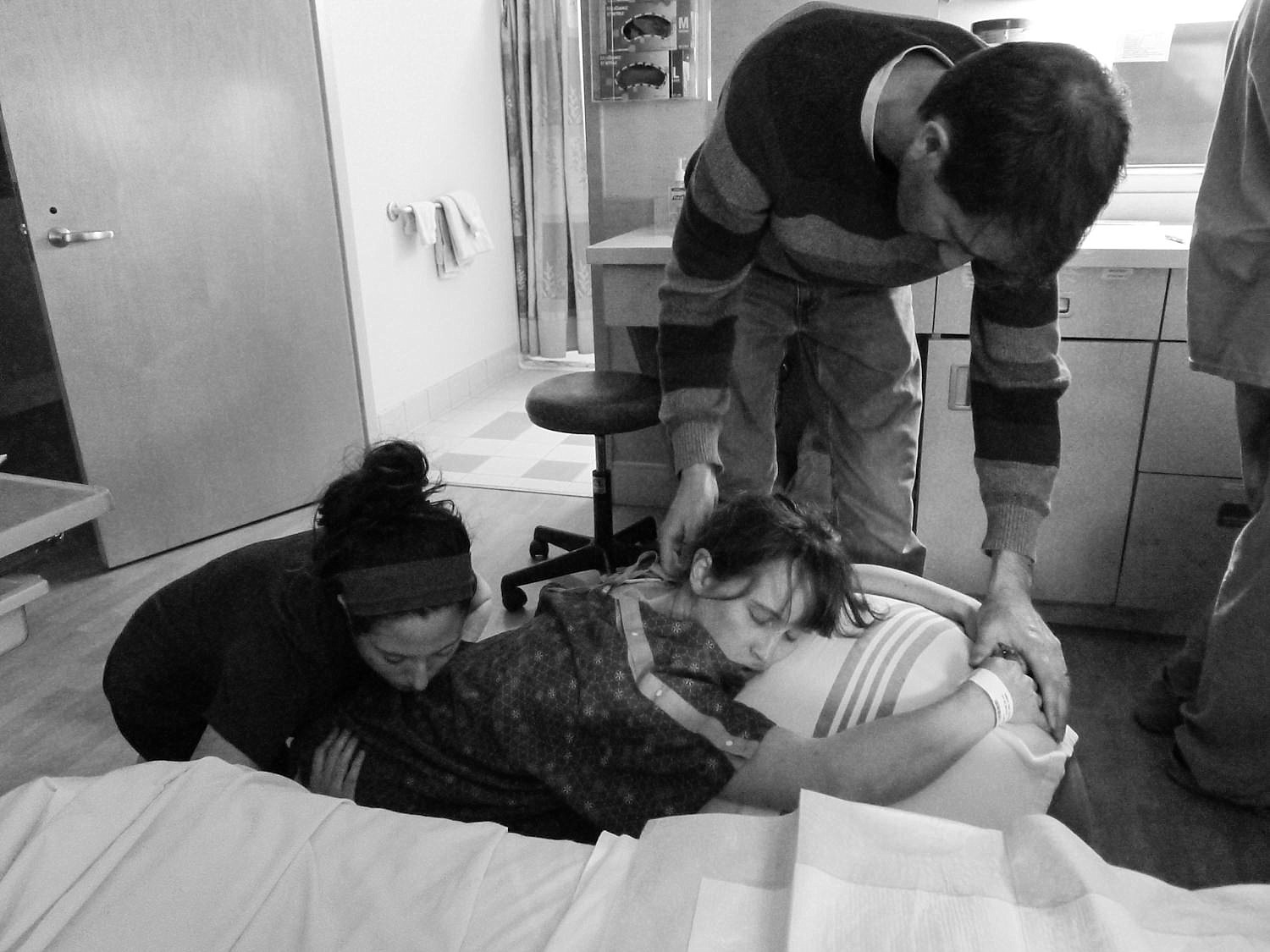  Woman in labor at the hospital, surrounded by her husband, doula and nurses. 