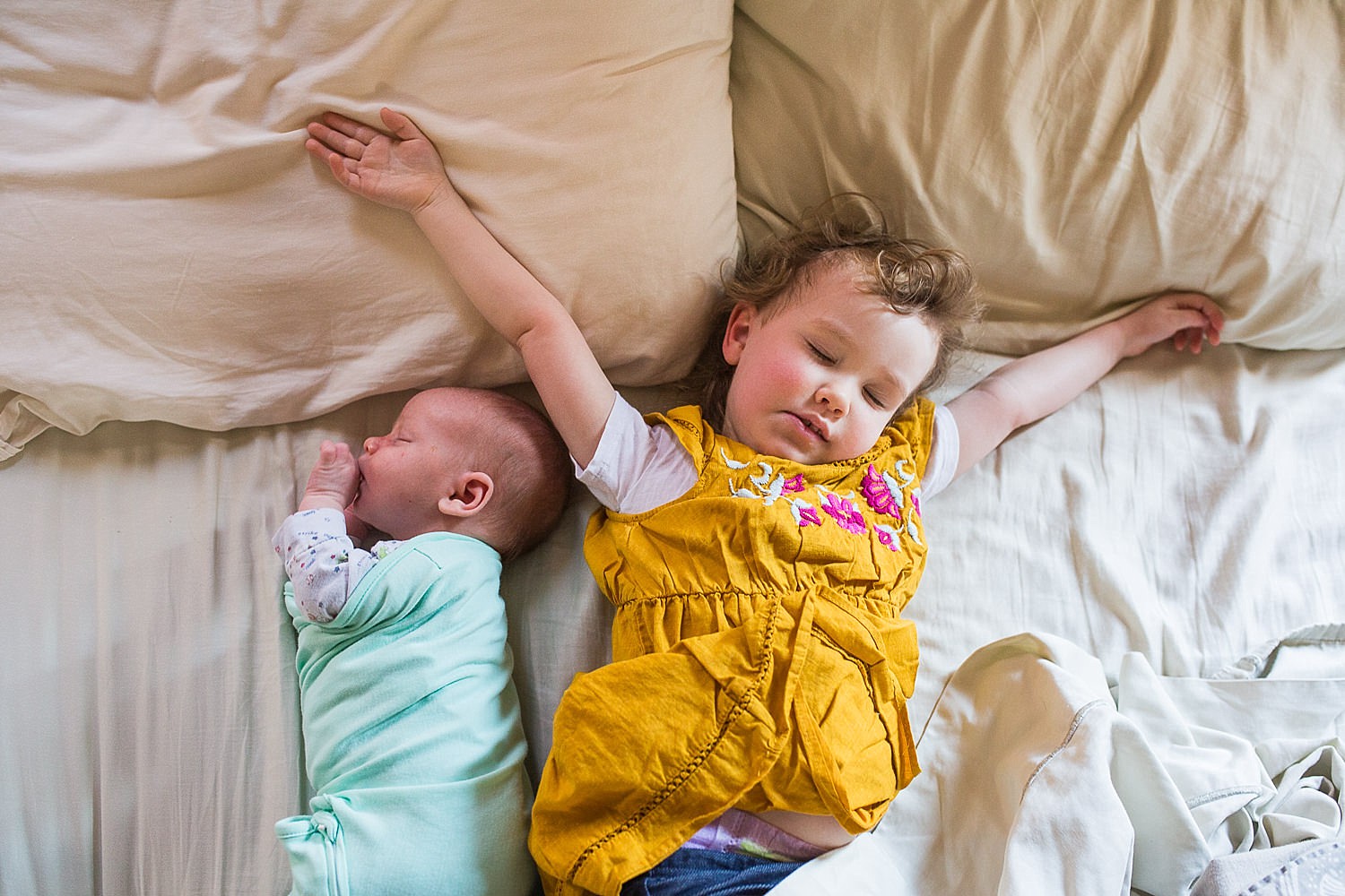  Photo of a newborn baby and his toddler big sister napping together in bed. 