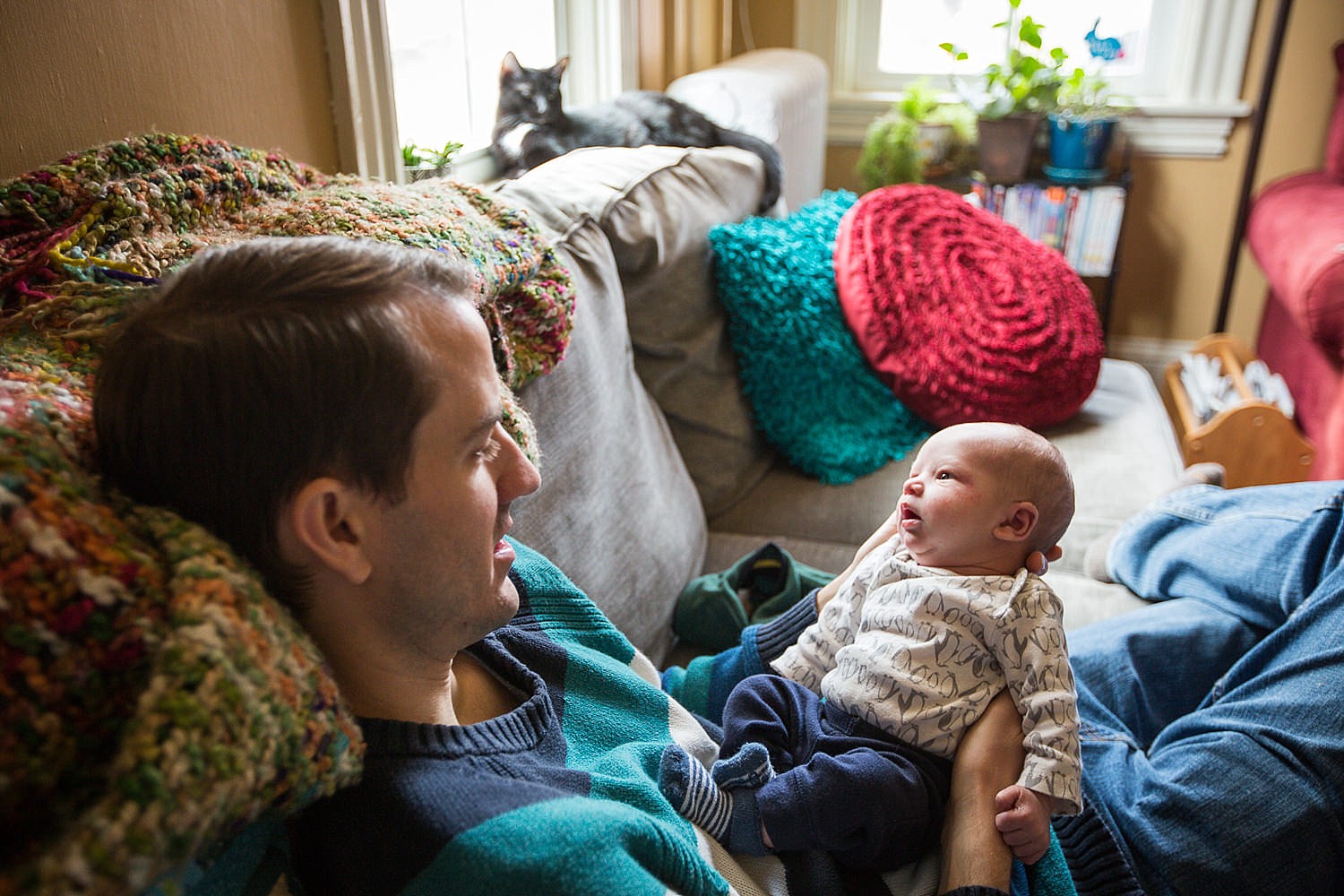  Photo of a father holding his newborn baby boy on the couch in their home. 