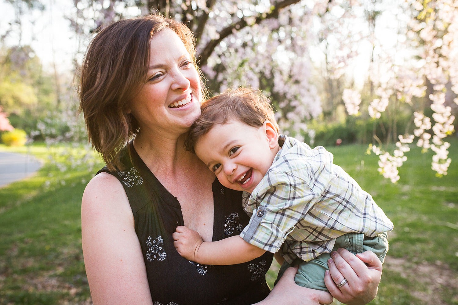  Happy photo of a mother holding her toddler son in front of a flowering cherry tree at Buchmiller Park. 