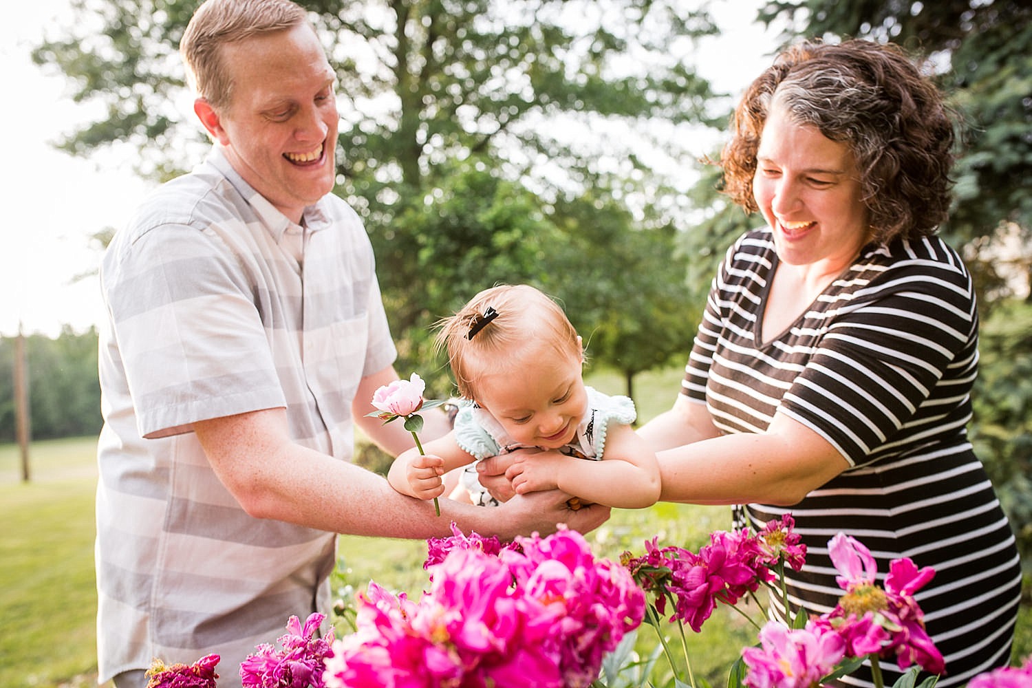  Photo of parents swinging their one year old daughter over some pink peony flowers. 