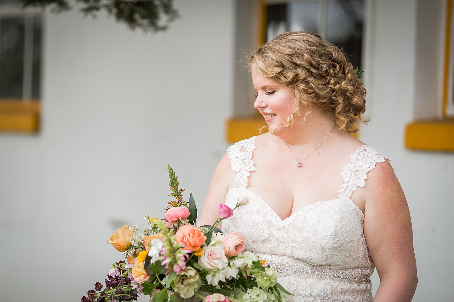  Photo of a bride with blonde hair and ringlets blowing in the wind as she looks down at her bouquet of flowers. 