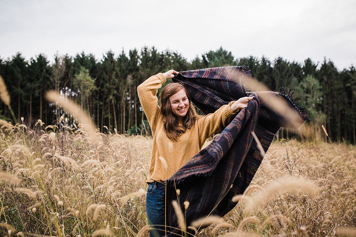  Young woman wrapped in a blanket standing in a field of golden grasses. 