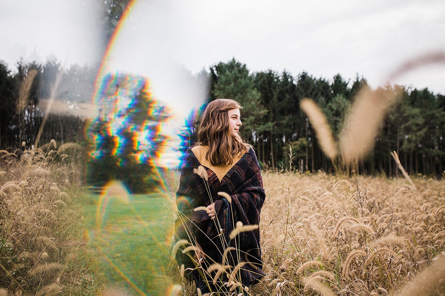  Young woman wrapped in a blanket standing in a field of golden grasses. 