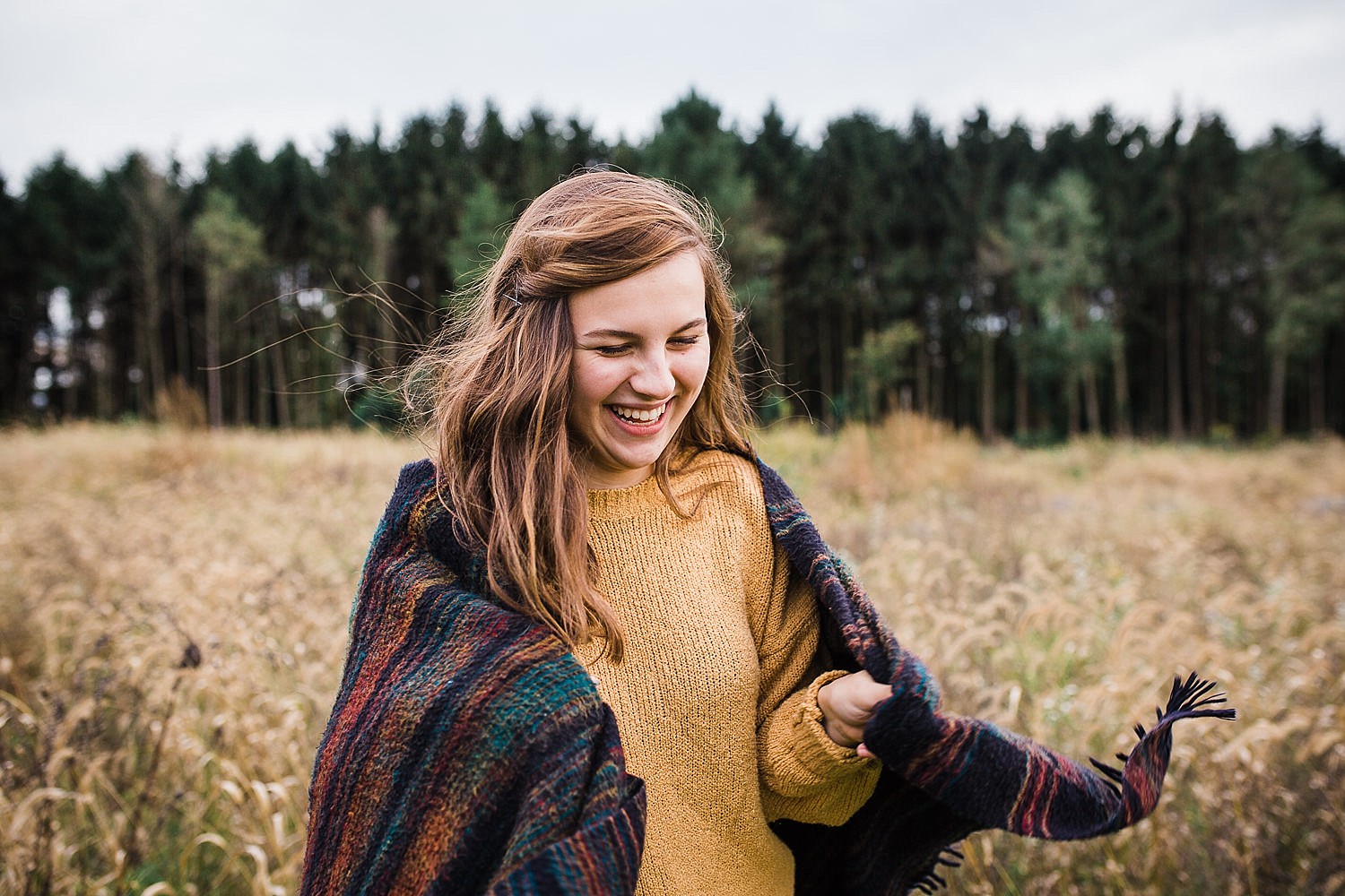  Young woman wrapped in a blanket standing in a field of golden grasses. 