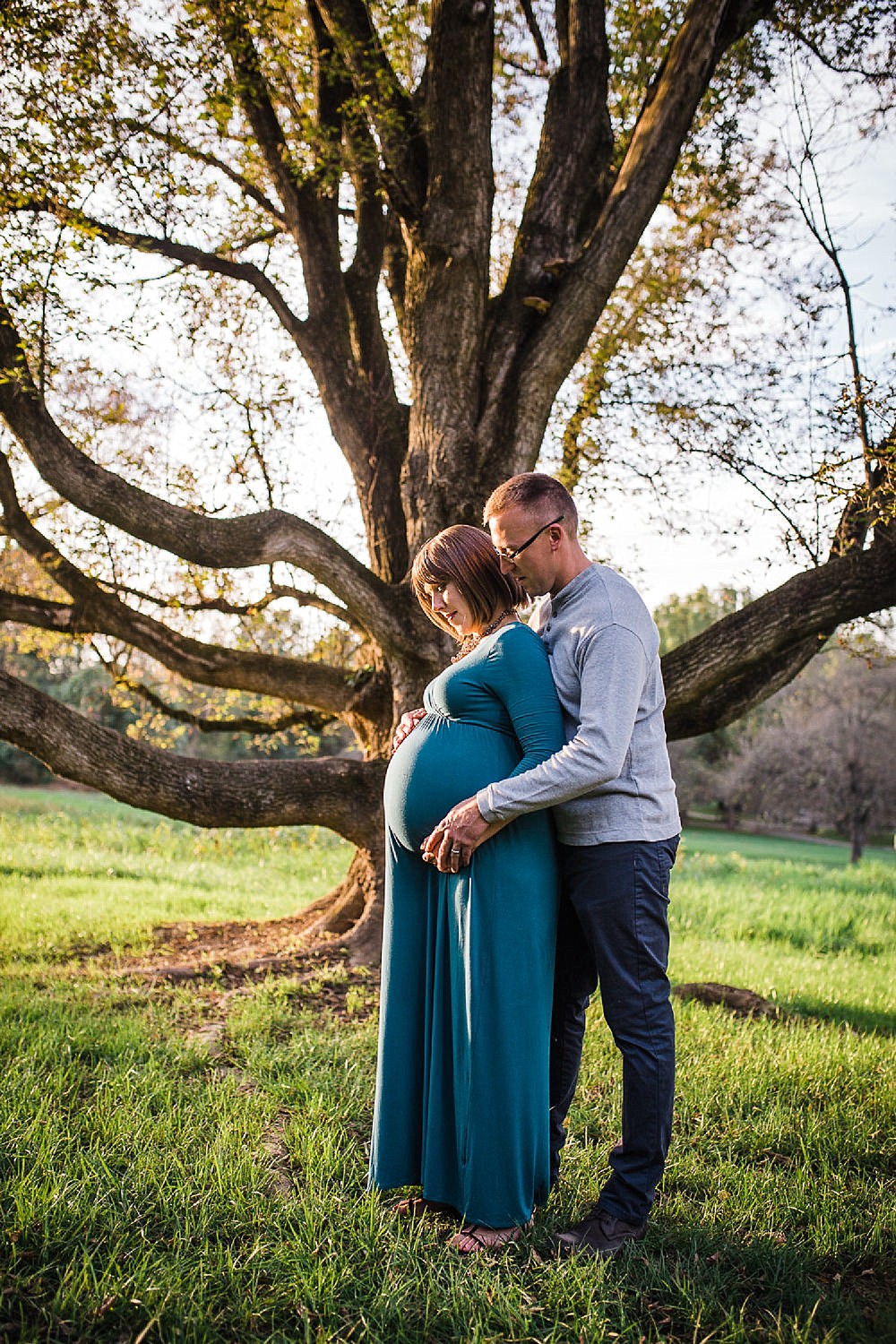  Photo of a pregnant woman in a teal dress and her husband smiling in the golden sunlight 