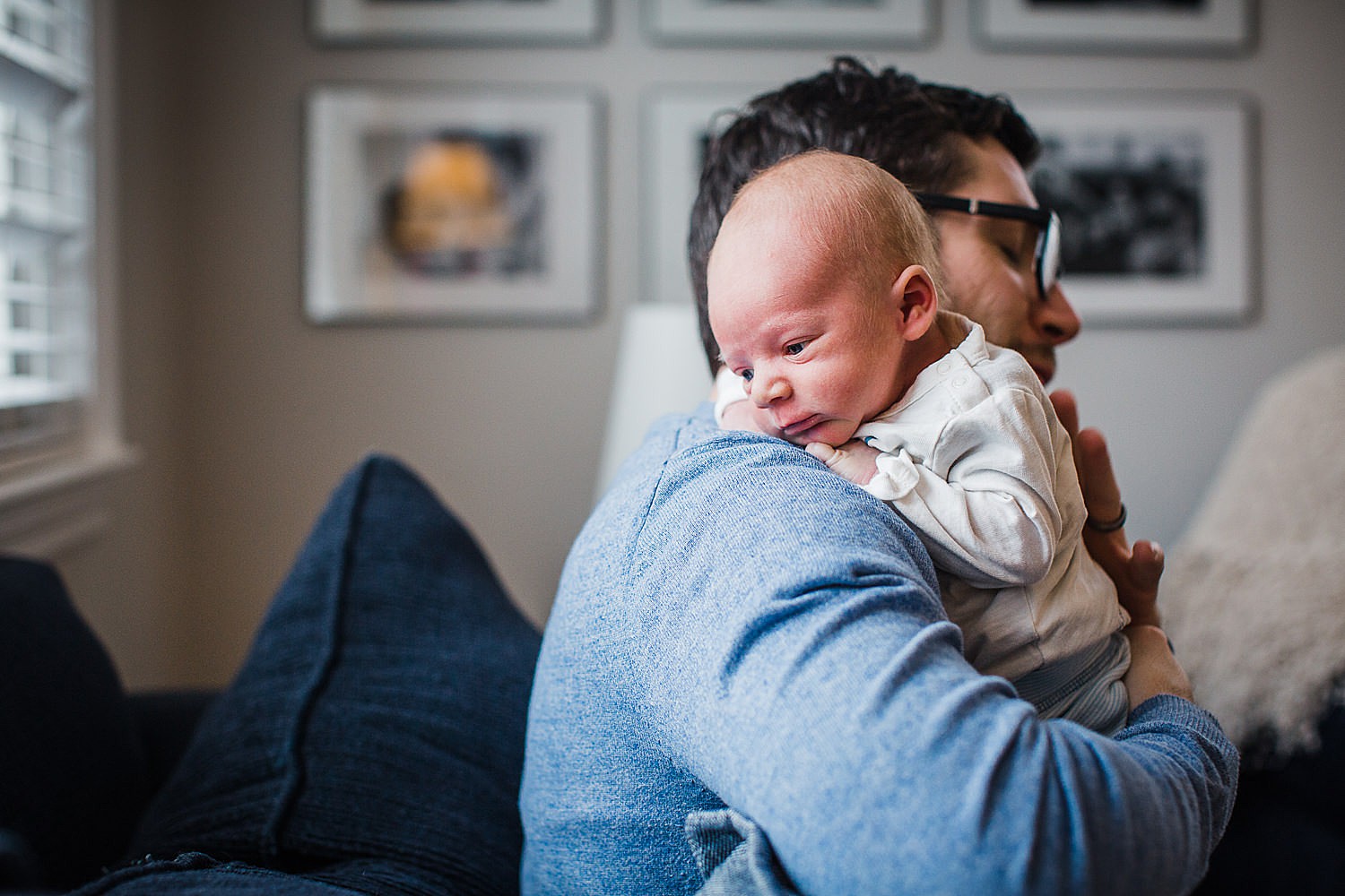  Photo of a young father holding his newborn son on a blue sofa in his home. 