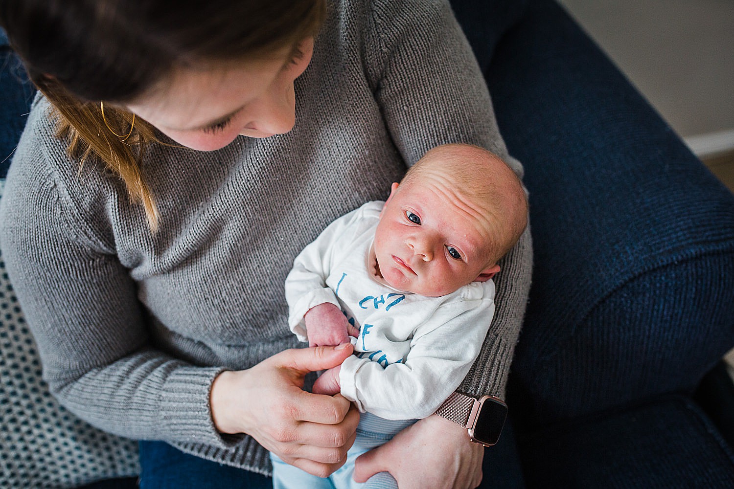  Photo of a mother holding her newborn son on a couch in her home. 