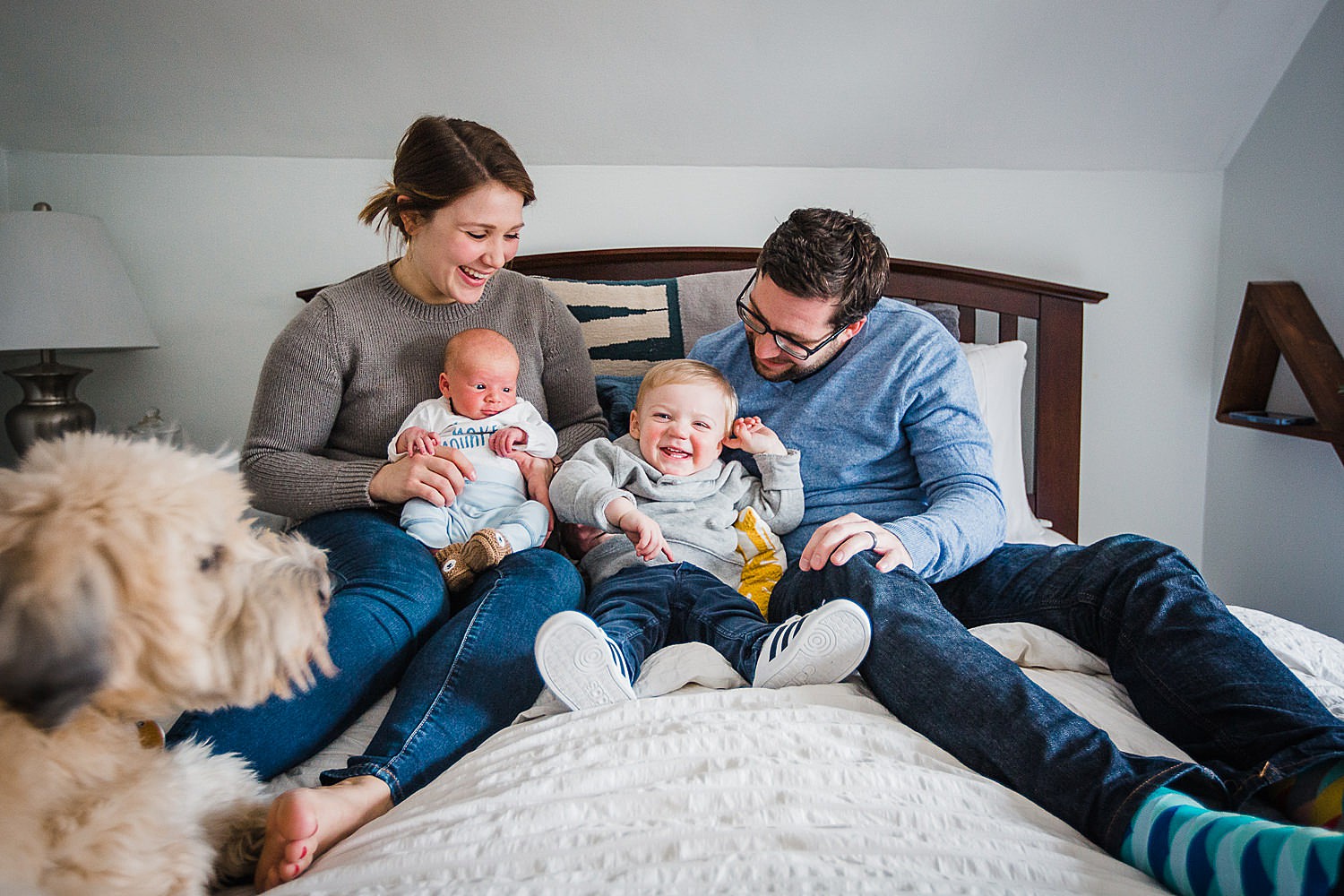  Photo of a family sitting on the bed and laughing, along with the family dog. 