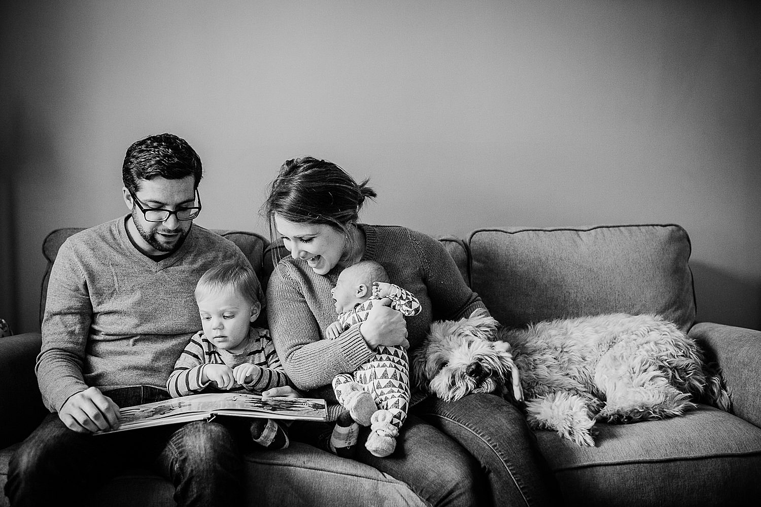  Photo of a young family reading a book together on the couch. 