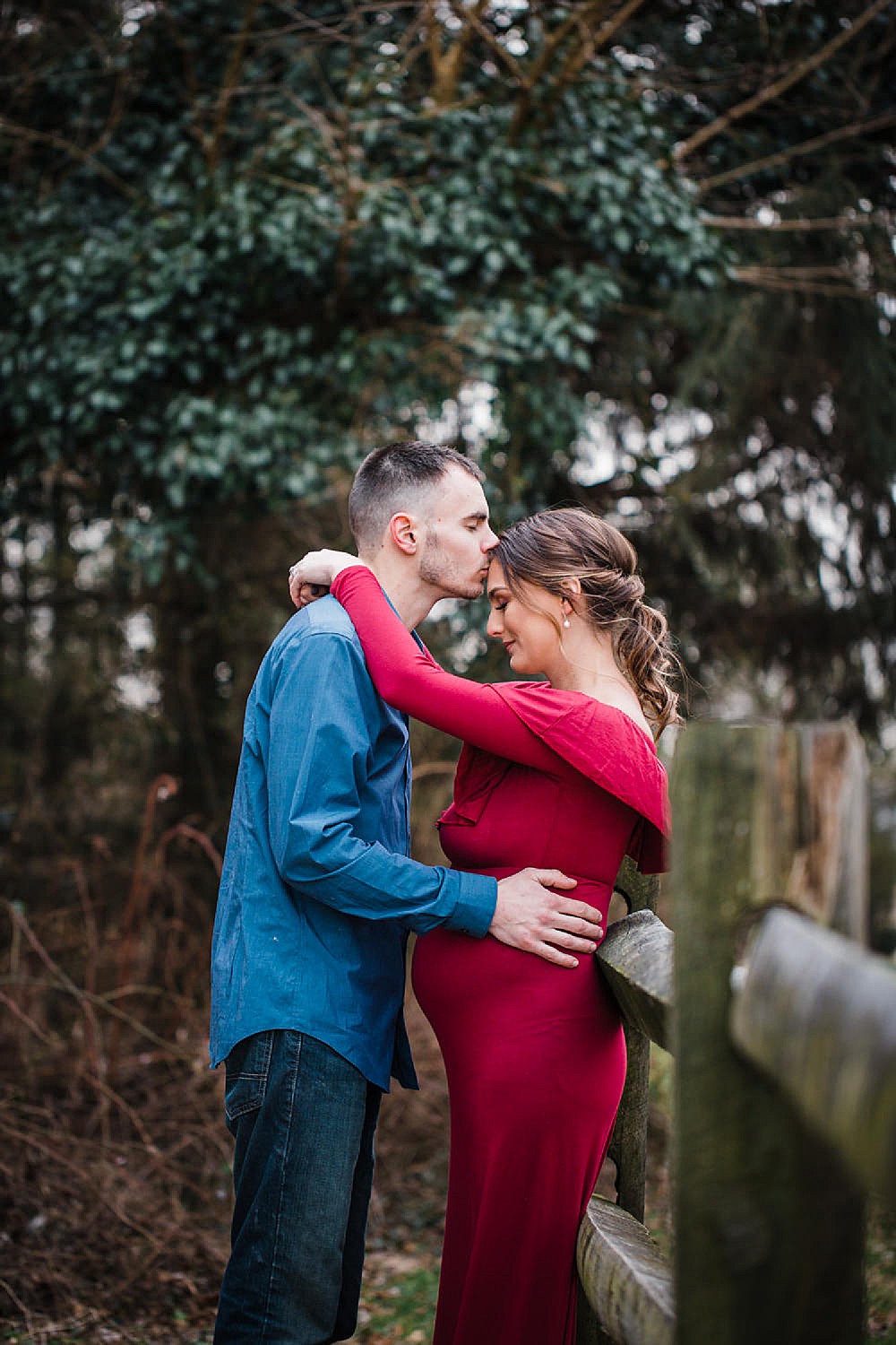  Photo of a pregnant woman in a red dress with her arms wrapped around her husband. 