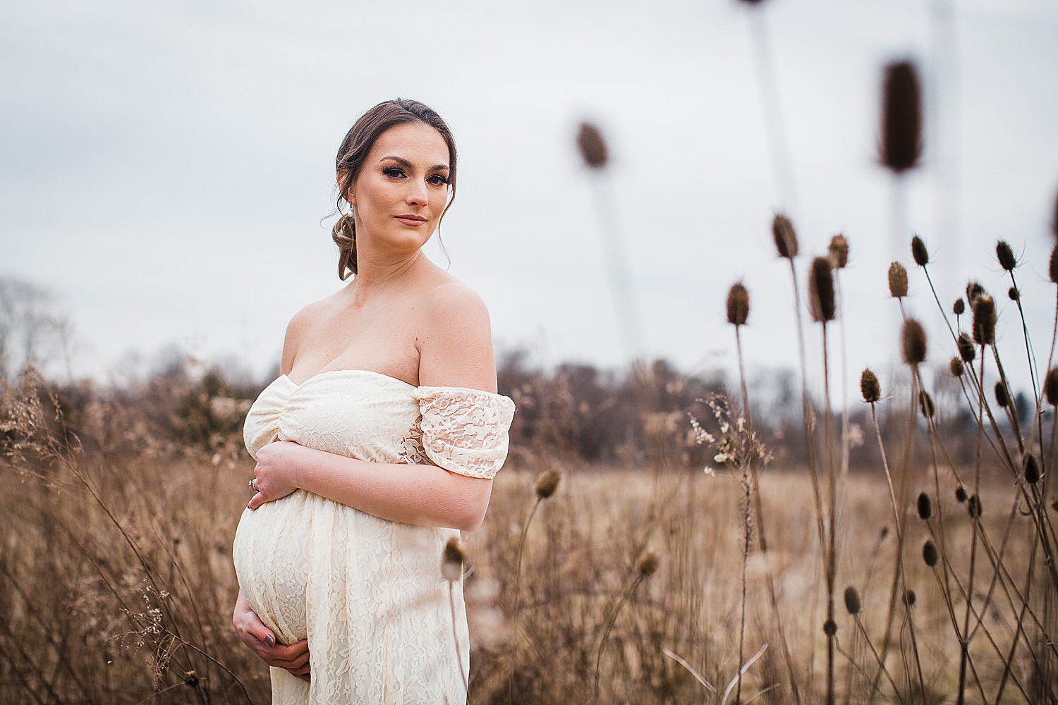  Photo of a young beautiful pregnant woman standing in a field wearing a white dress. 