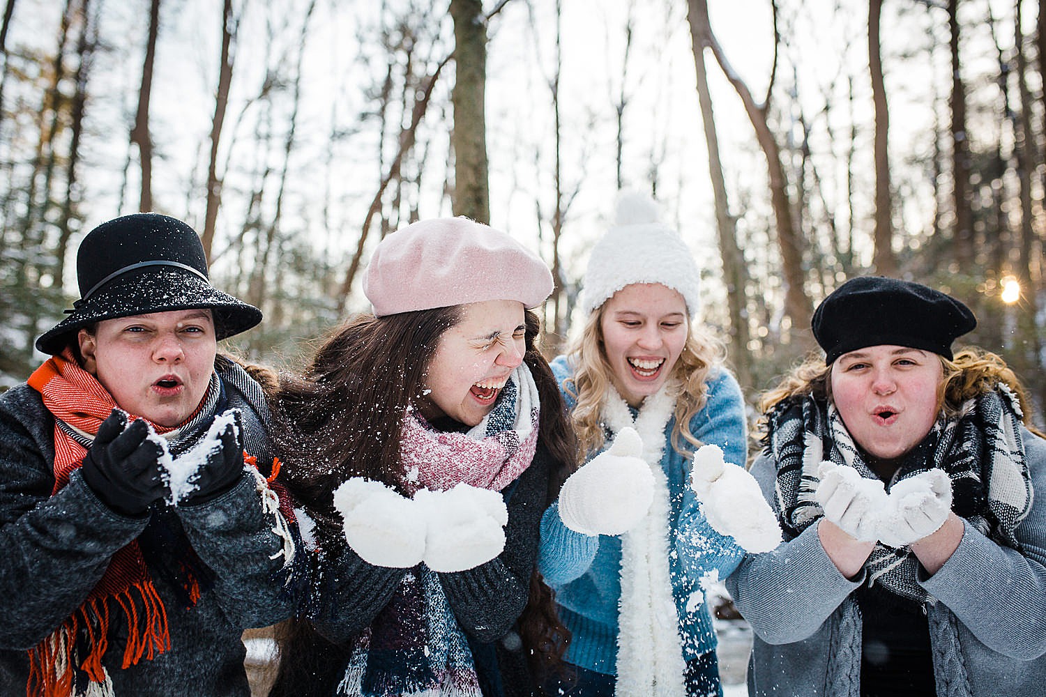  Photo of four young women standing in a row laughing in a wintery forest. 