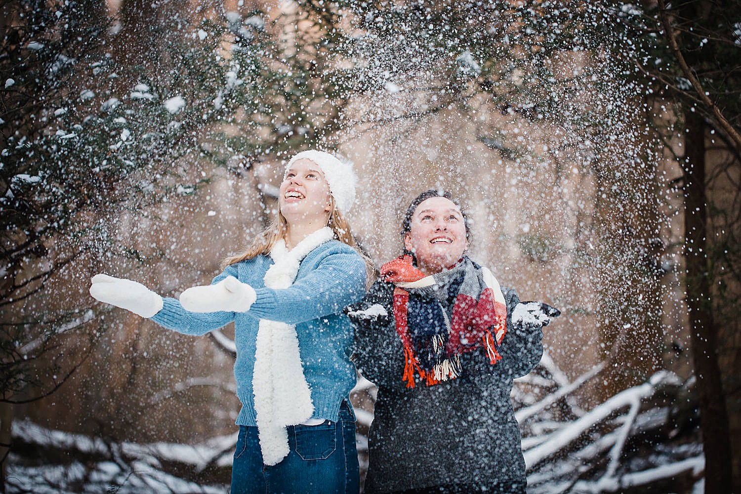 Photo of two young women throwing snow in the air in a wintery forest. 