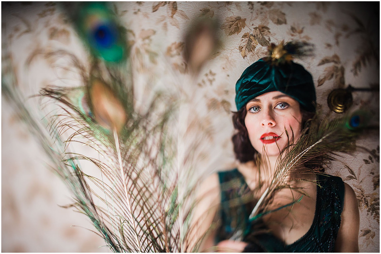  Photo of a glamorous young brunette woman wearing a green vintage flapper dress and a green velvet turban and peacock feathers. 