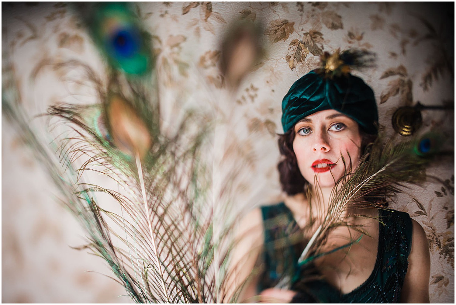 Photo of a glamorous young brunette woman wearing a green vintage flapper dress and a green velvet turban and peacock feathers.