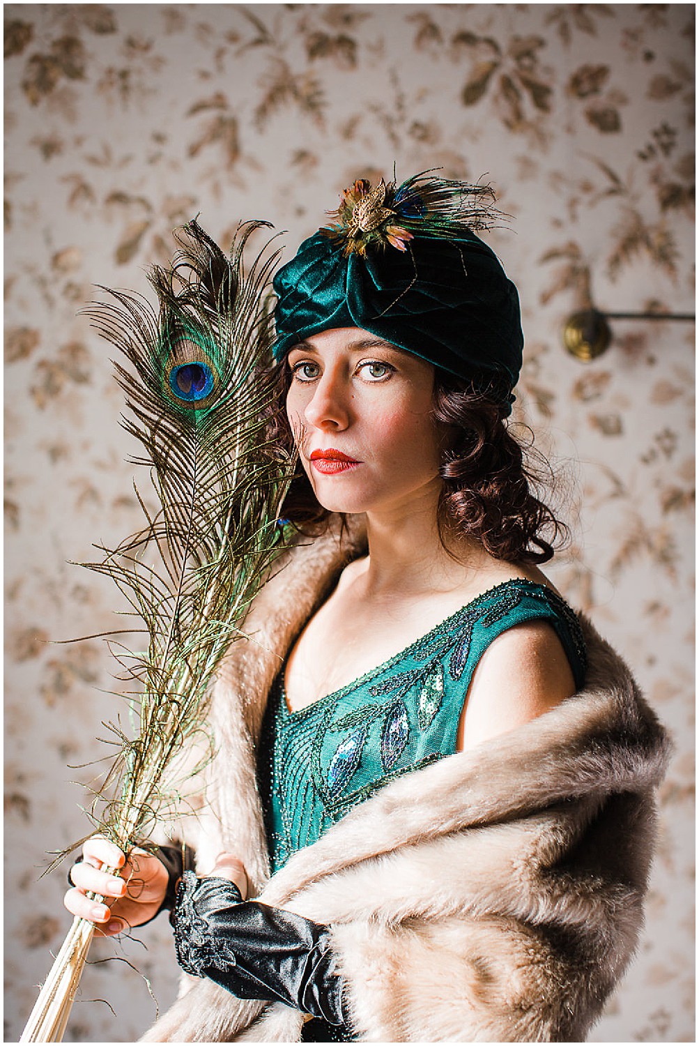 Photo of a glamorous young brunette woman wearing a green vintage flapper dress and a green velvet turban and peacock feathers.