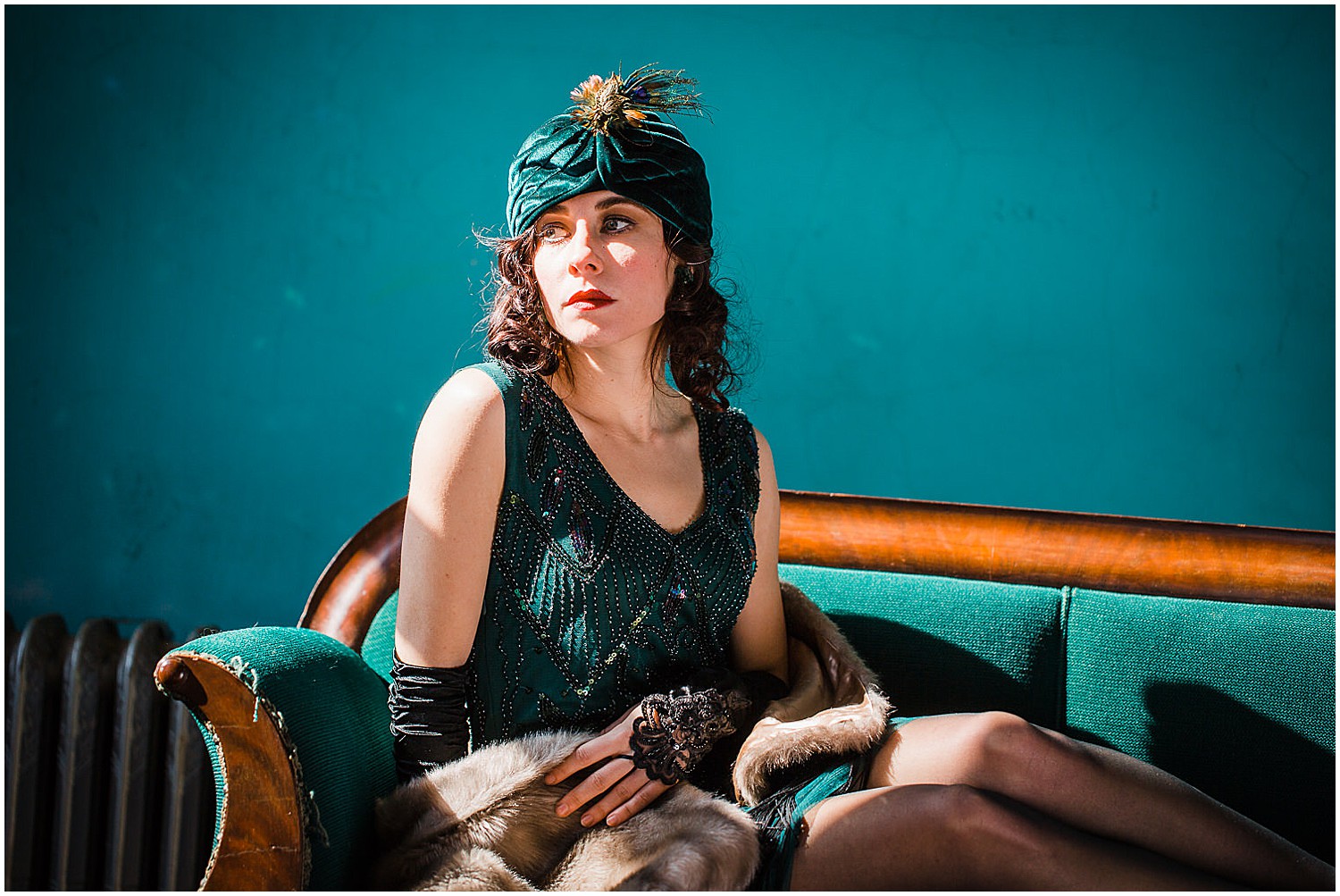  Photo of a glamorous young brunette woman wearing a green vintage flapper dress and a green velvet turban and peacock feathers. 