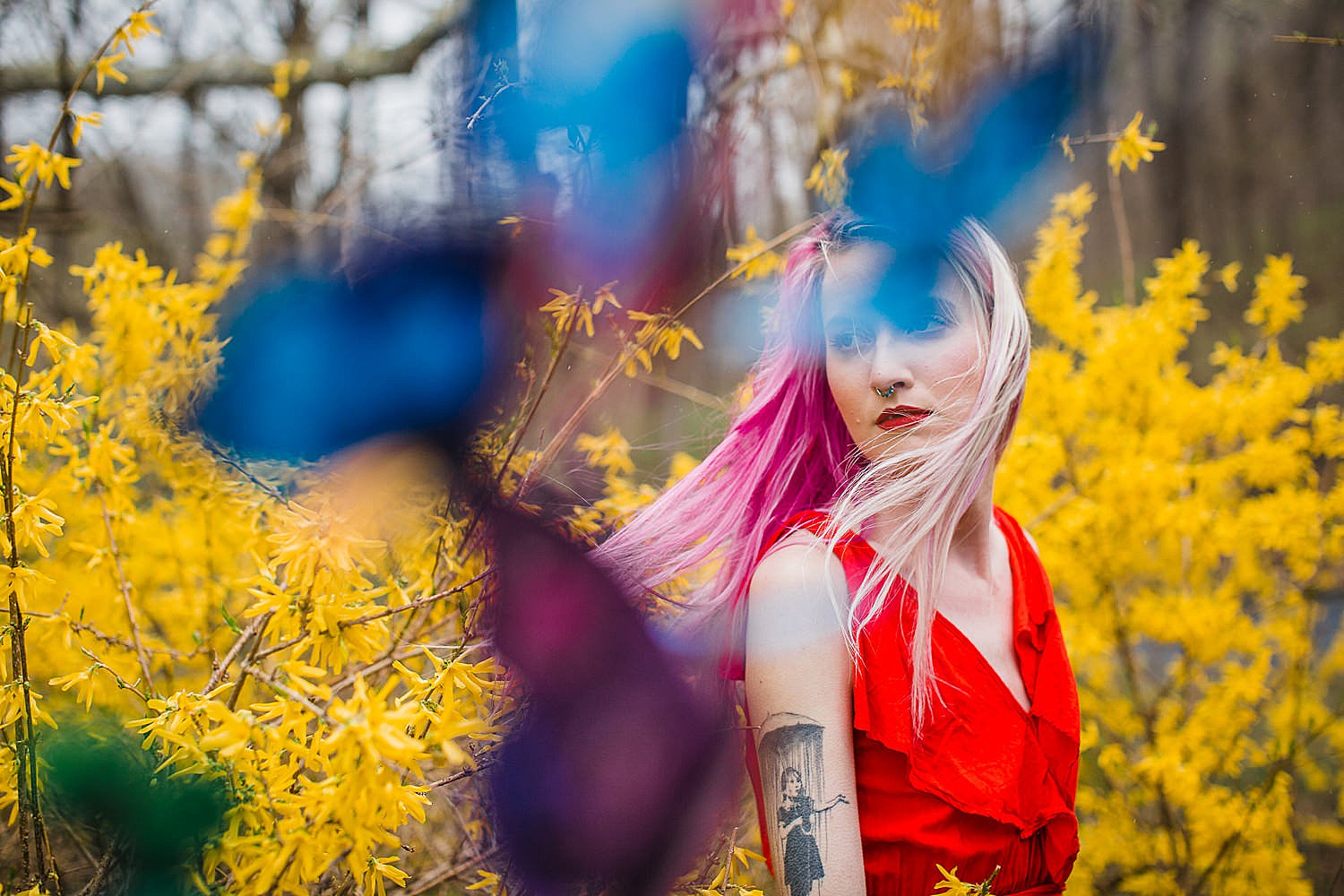  Portrait photo of a young woman wearing a bright red dress standing in front of a yellow forsythia bush surrounded by colorful butterflies. 