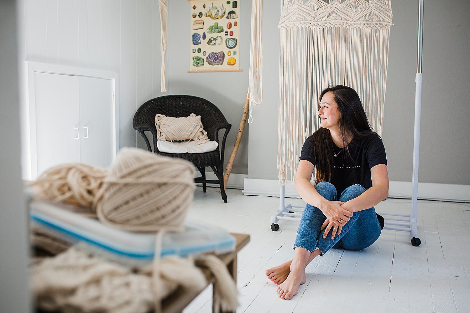  Photo of a young woman sitting in a bright studio space creating macrame art. 