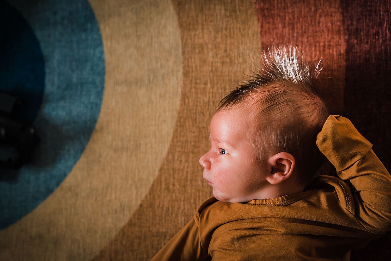 newborn baby lying on a rainbow rug