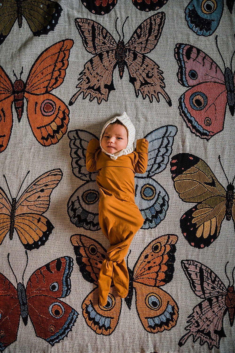 Newborn baby lies on a butterfly blanket from Urban Outfitters