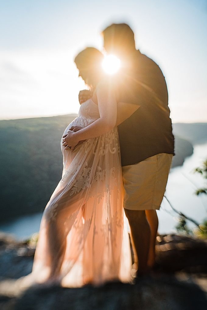 A couple stands on a rocky overlook at sunset