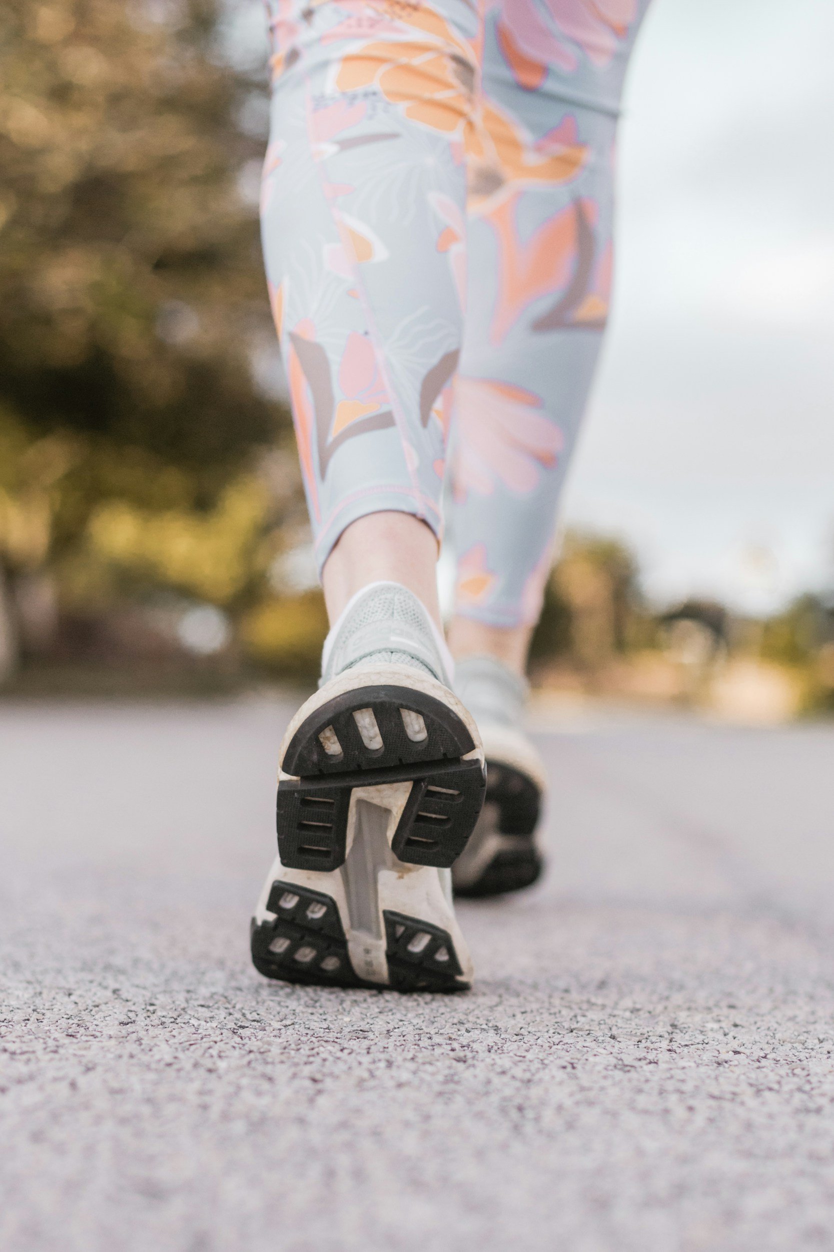 Close-up of a person roller skating outdoors on a paved surface, focusing on the bottom of their white skate and colorful floral patterned leggings.