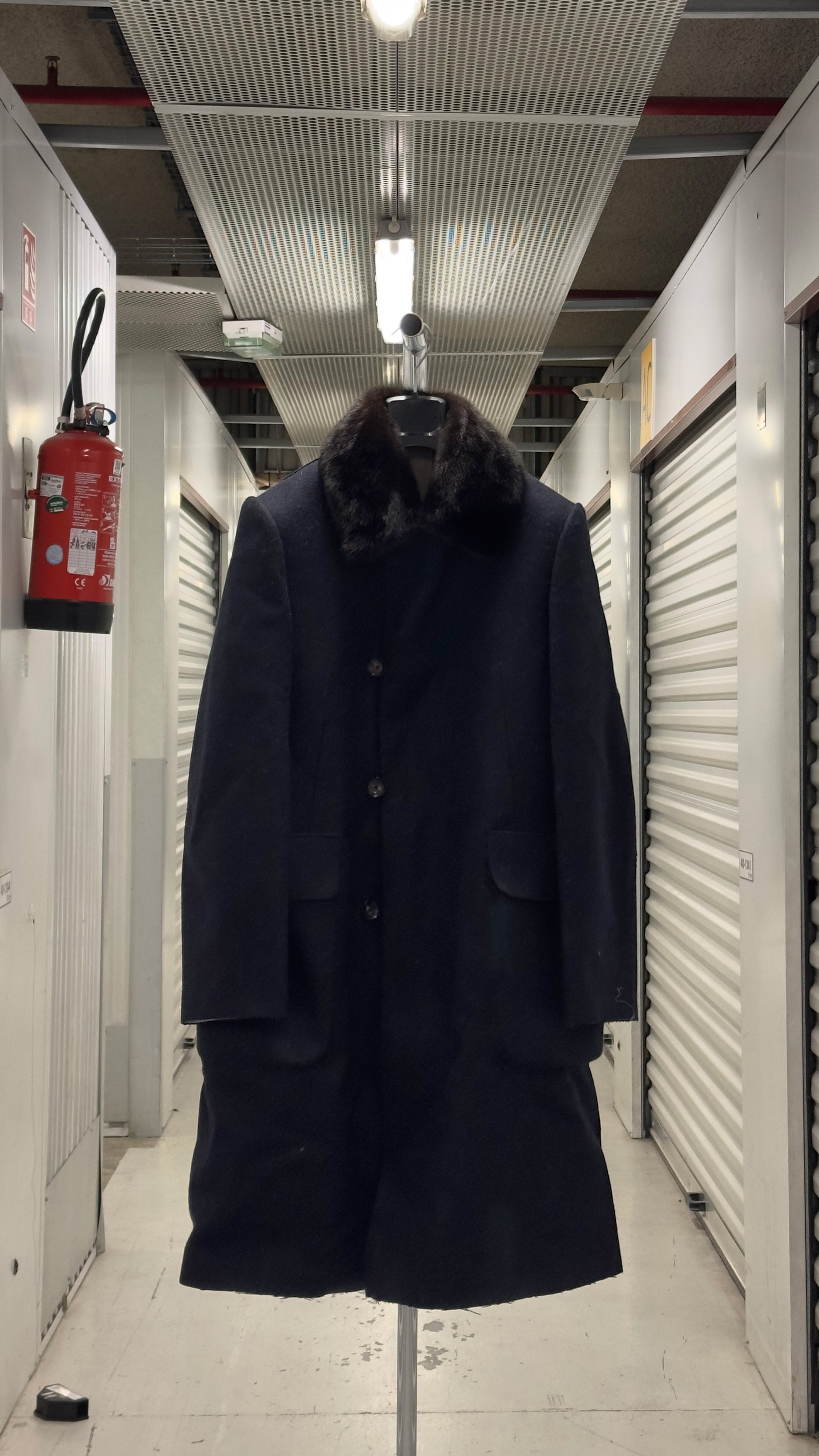 Manteau noir avec col en fourrure sur cintre dans un couloir de stockage