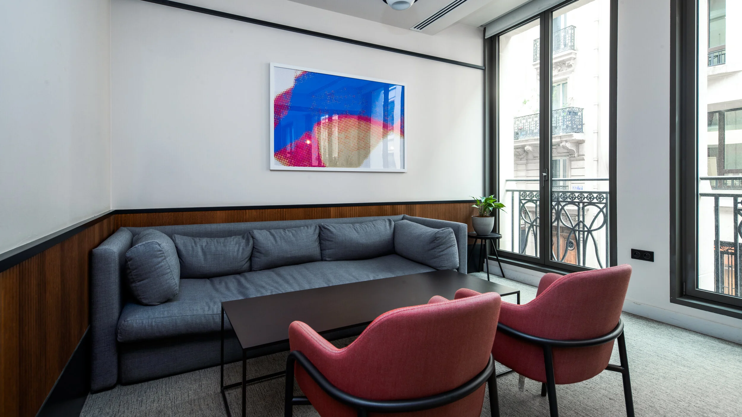 Modern living room with gray sofa, pink armchairs, black coffee table, artwork on the wall, and large windows with balcony view.
