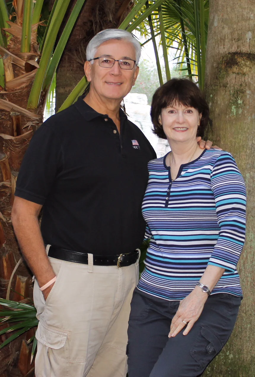 Husband and wife, Vince and Debbie Collier, pose for a picture in front of palm trees.