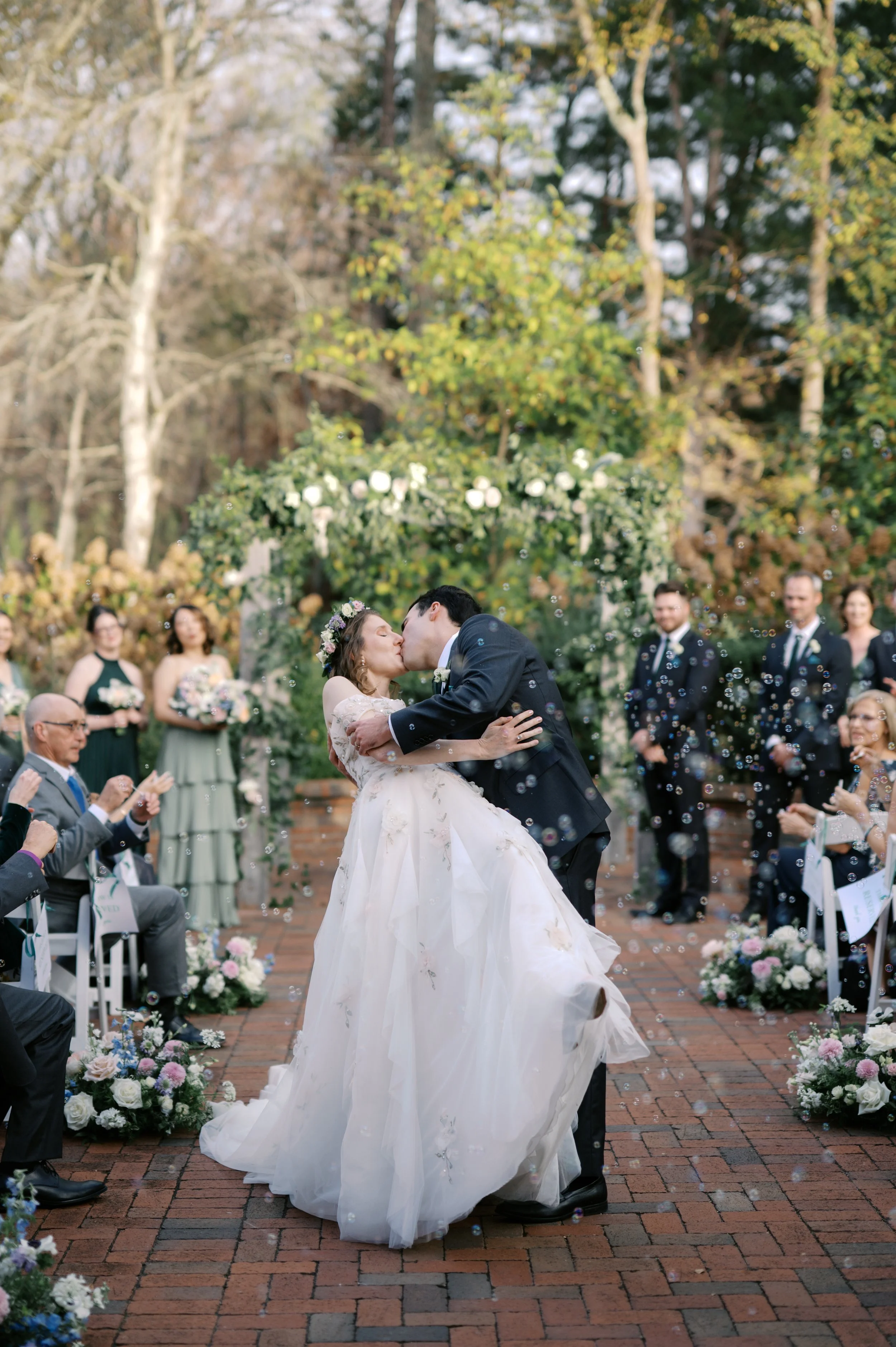 Bride and groom celebrating their first kiss surrounded by bubbles during a garden ceremony at The Barn of Chapel Hill
