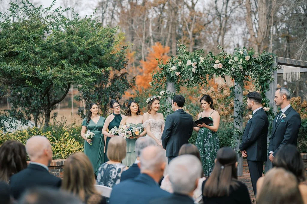Outdoor wedding ceremony at The Barn of Chapel Hill with couple exchanging vows beneath a garden arbor surrounded by guests