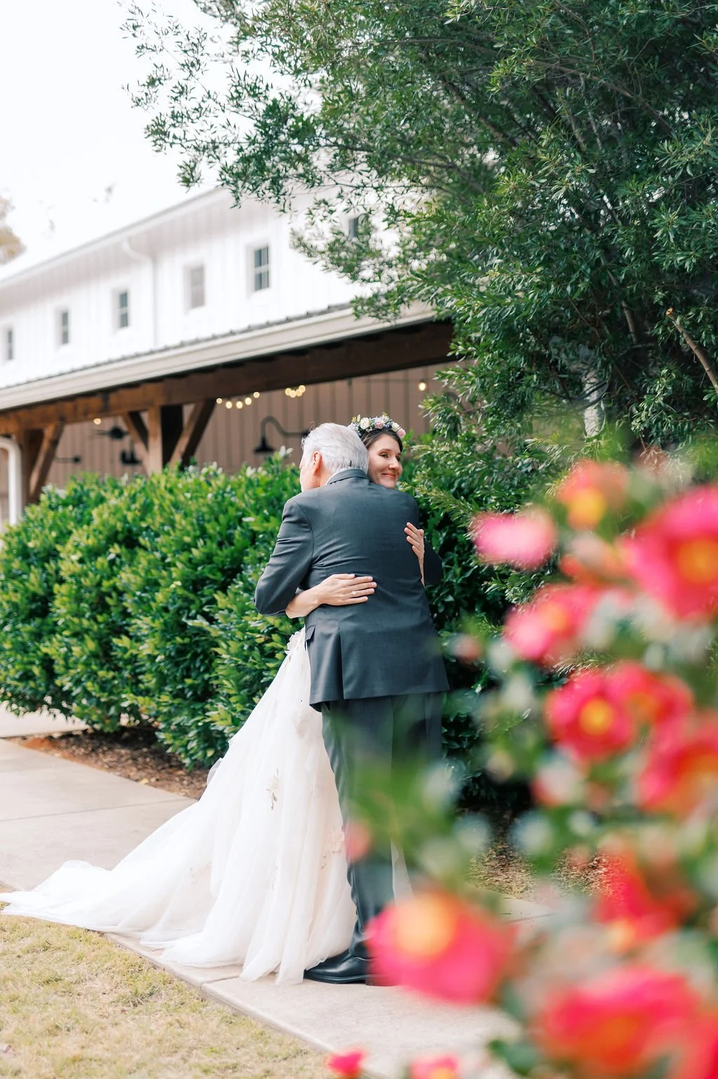 Bride hugging her father outside The Barn of Chapel Hill surrounded by lush garden greenery and flowers at a North Carolina wedding venue