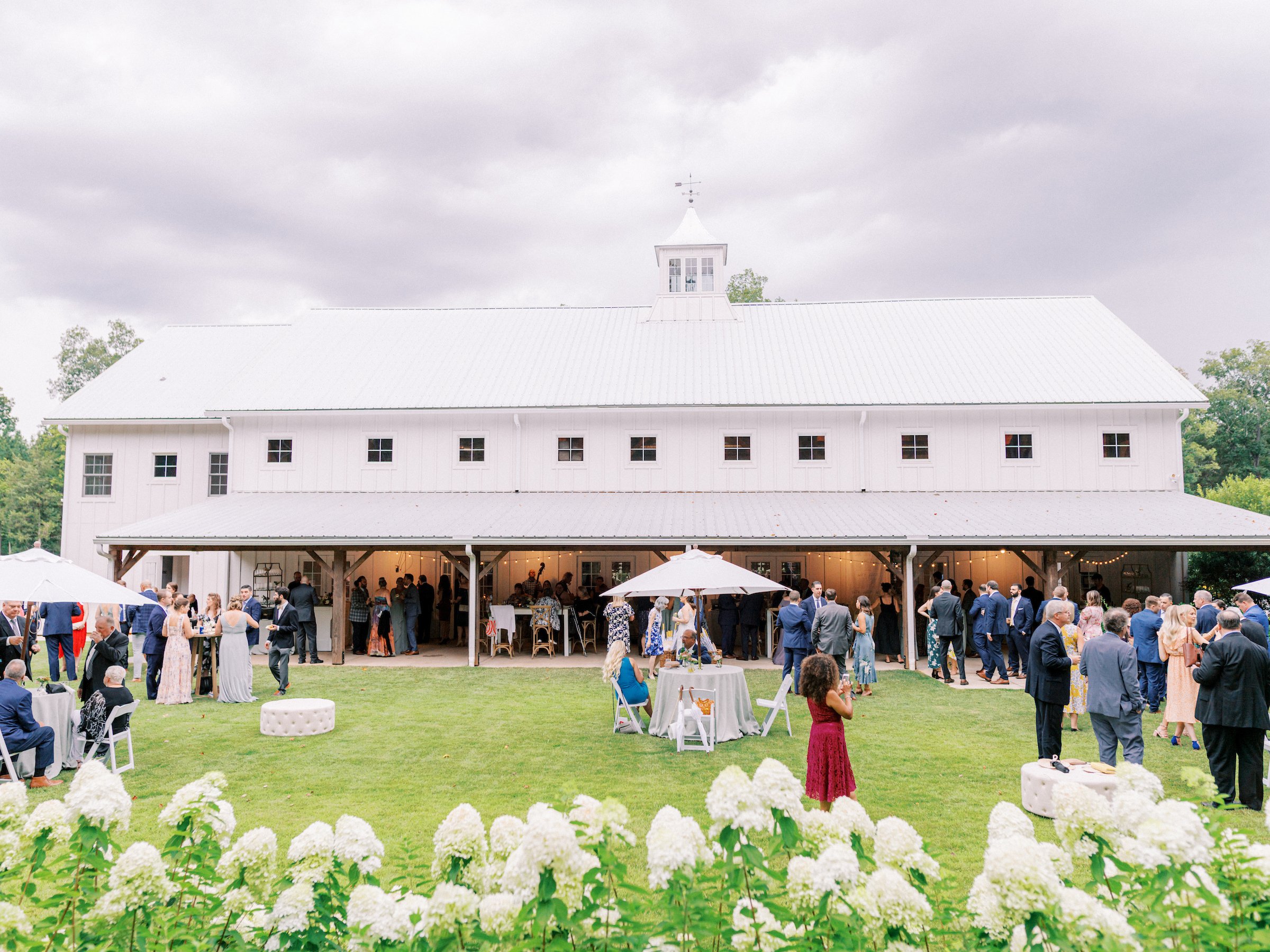 Wedding cocktail hour on the lawn outside The Barn of Chapel Hill with guests gathered around the historic white barn