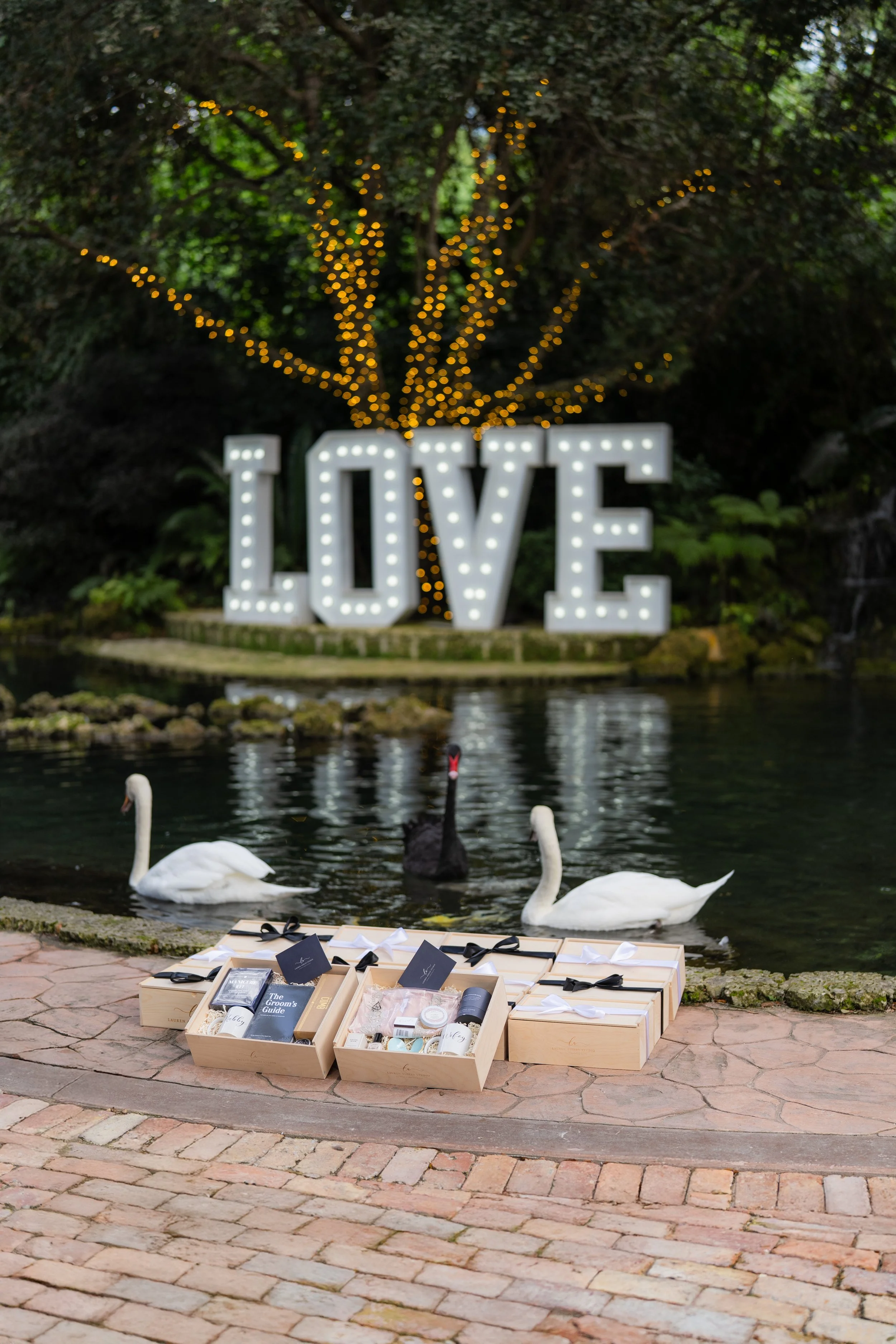 Custom wedding gift boxes displayed at an outdoor wedding with swans and illuminated LOVE sign