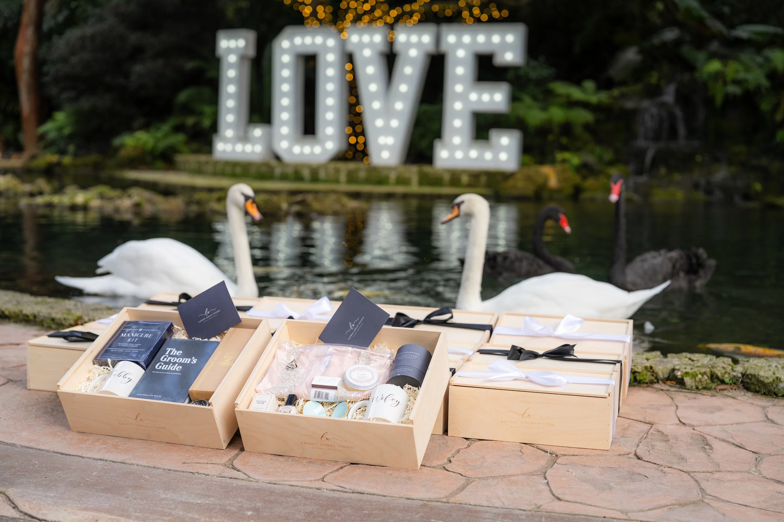 Luxury wedding welcome gift boxes in Miami styled at waterfront venue with swans and illuminated LOVE sign