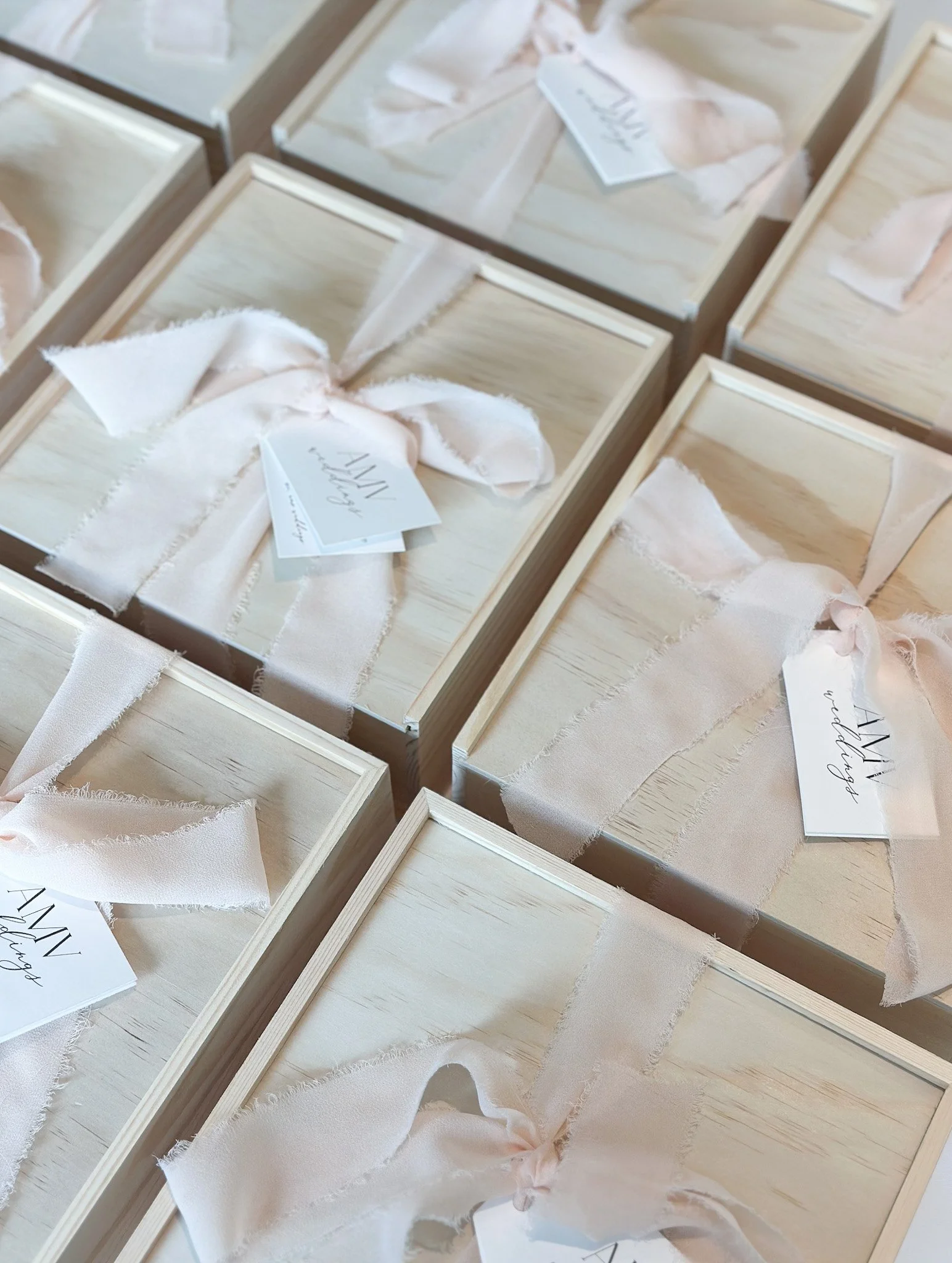 Multiple light wooden boxes with pale pink fabric ribbons and tags inside.