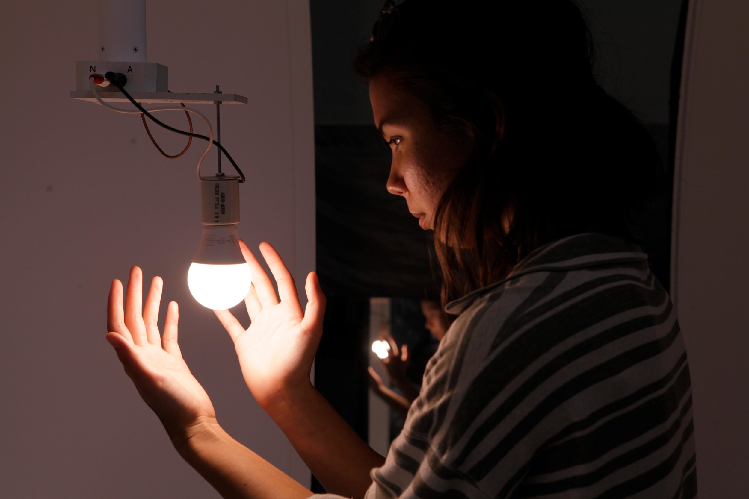 A young female university student wrapping her hands around an LED light bulb attached to a goniophotometer..jpg