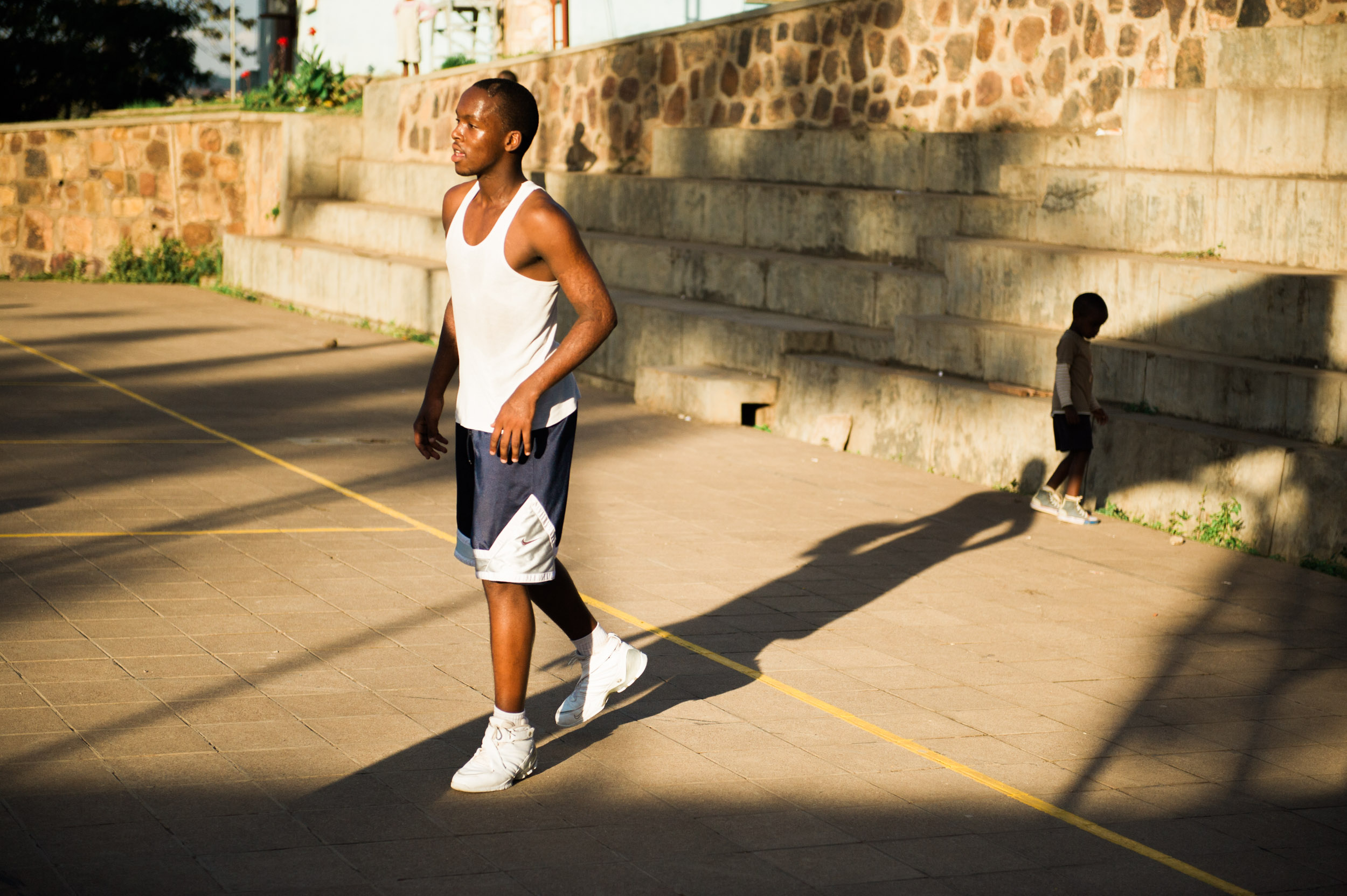  A young boy stands near a game of pick-up basketball in Kigali. 