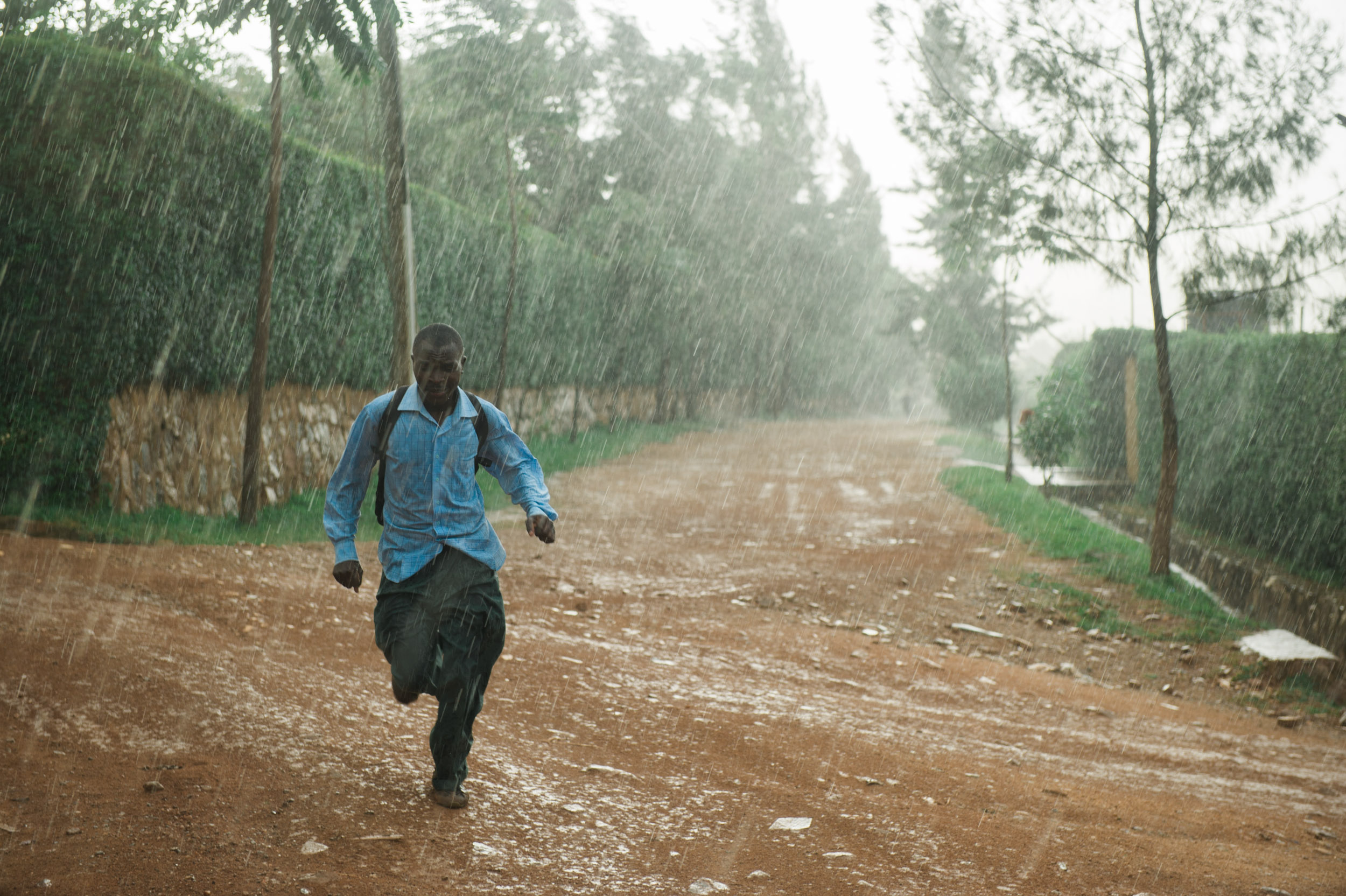  A young man runs home during a wet afternoon in the rainy season, Kigali. 